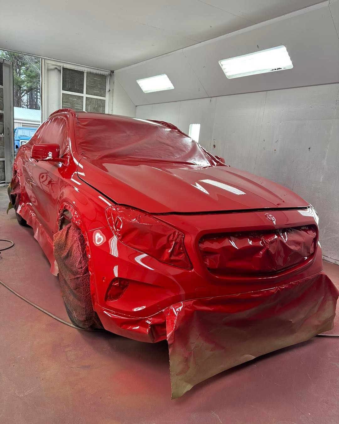 A red car is being painted in a garage.