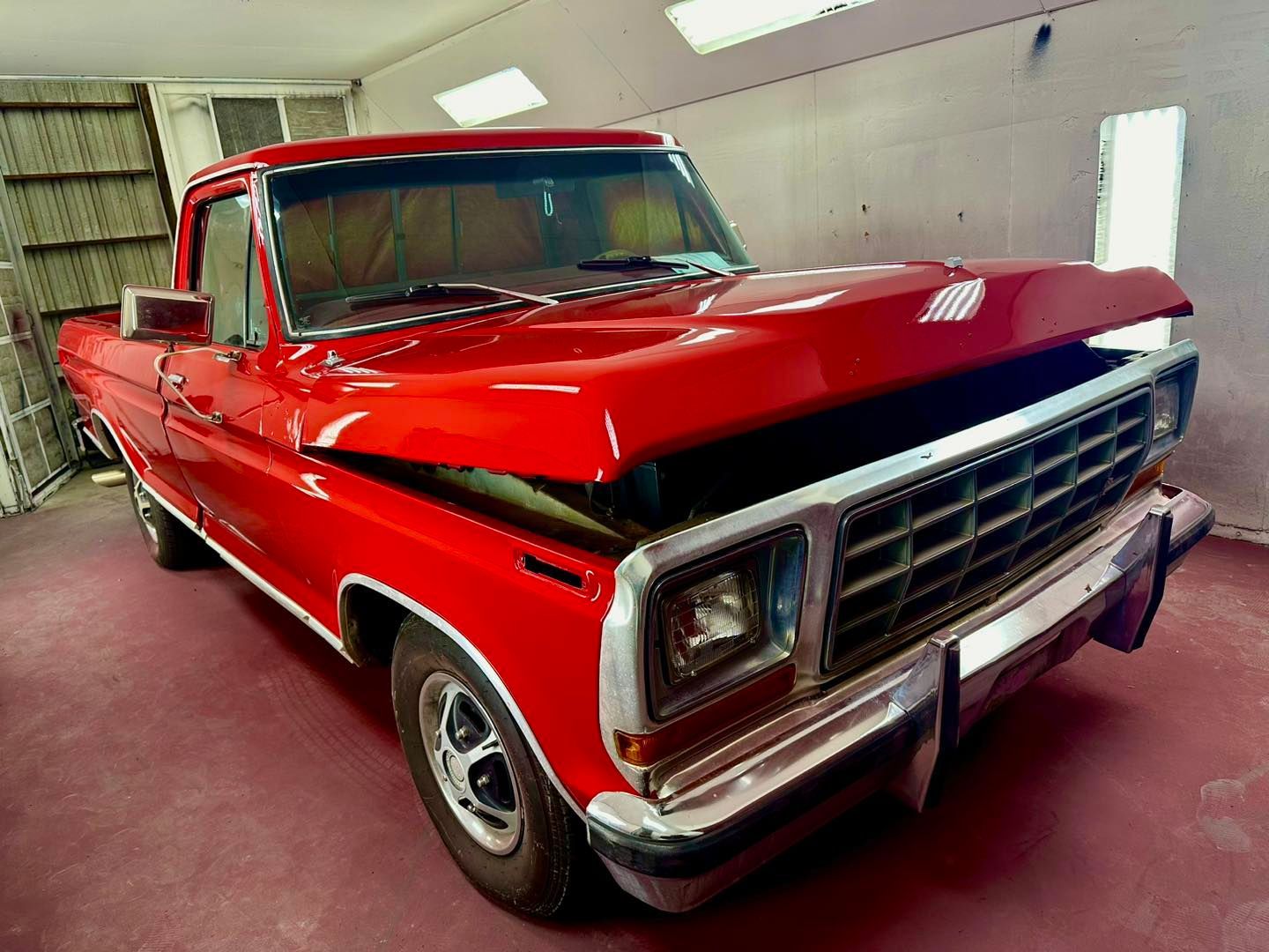 A red truck with its hood open is parked in a garage.