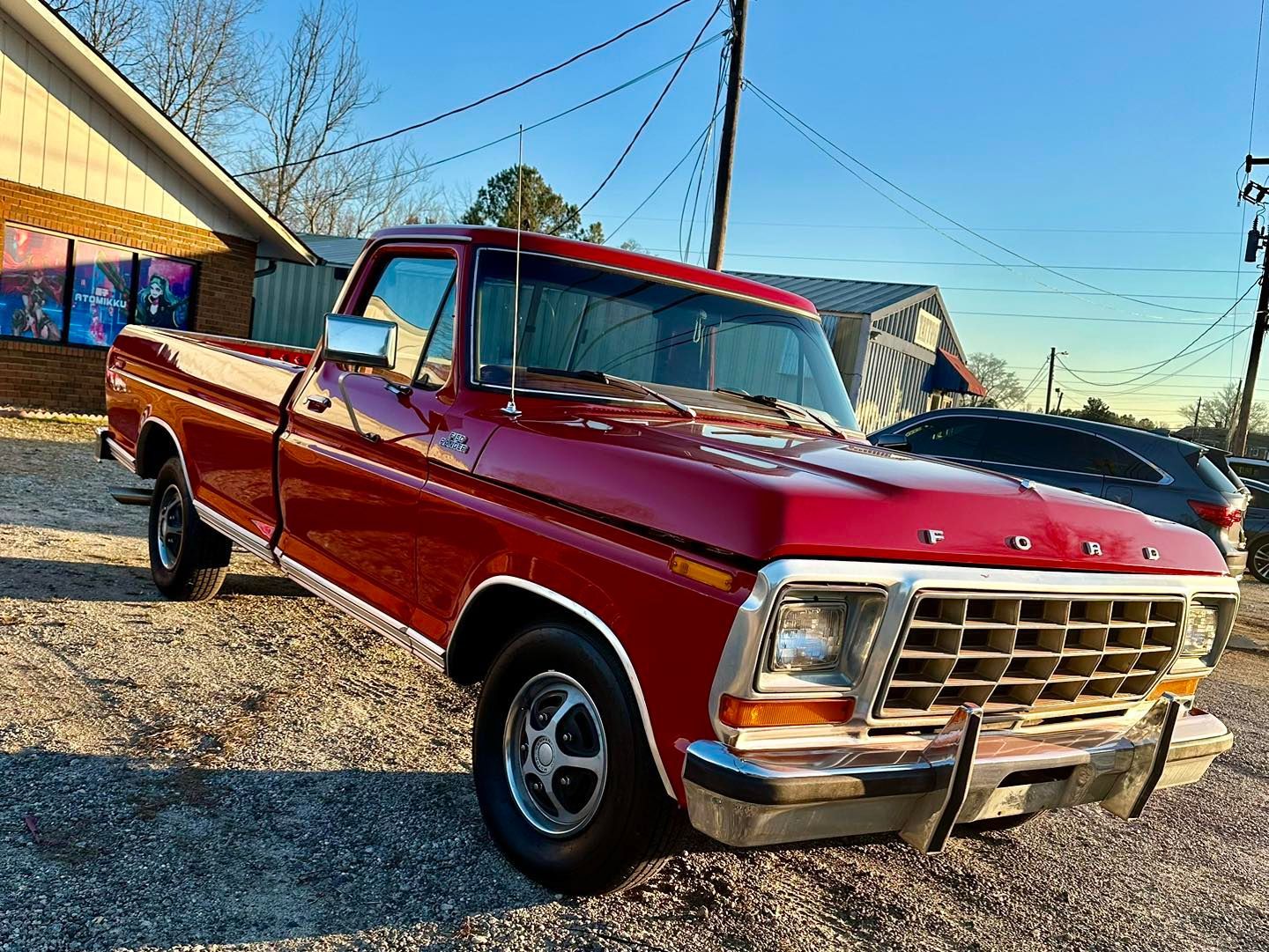 A red ford truck is parked in a gravel lot in front of a building.