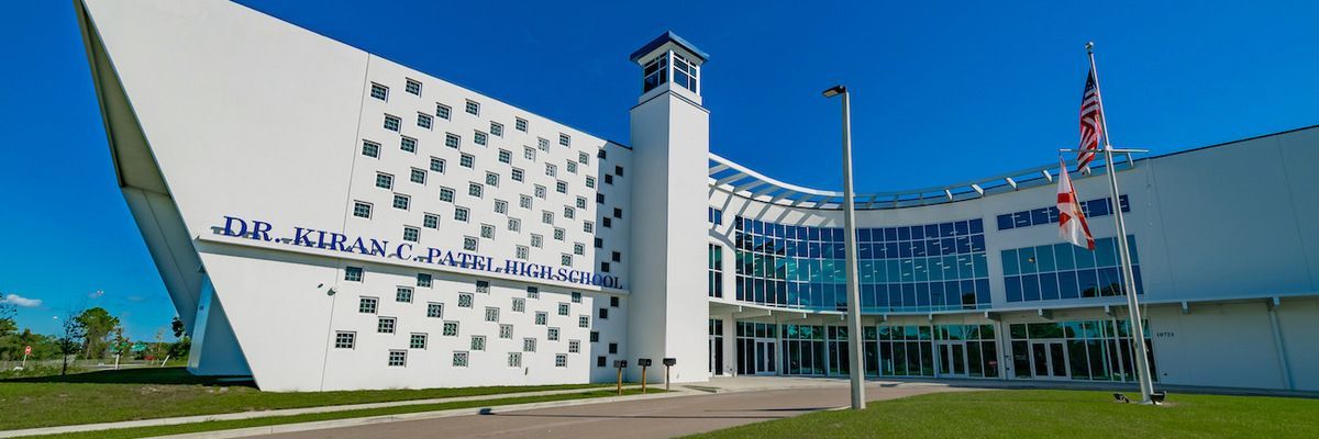 Modern glass-front airport terminal with a control tower, blue sky, and flags outside