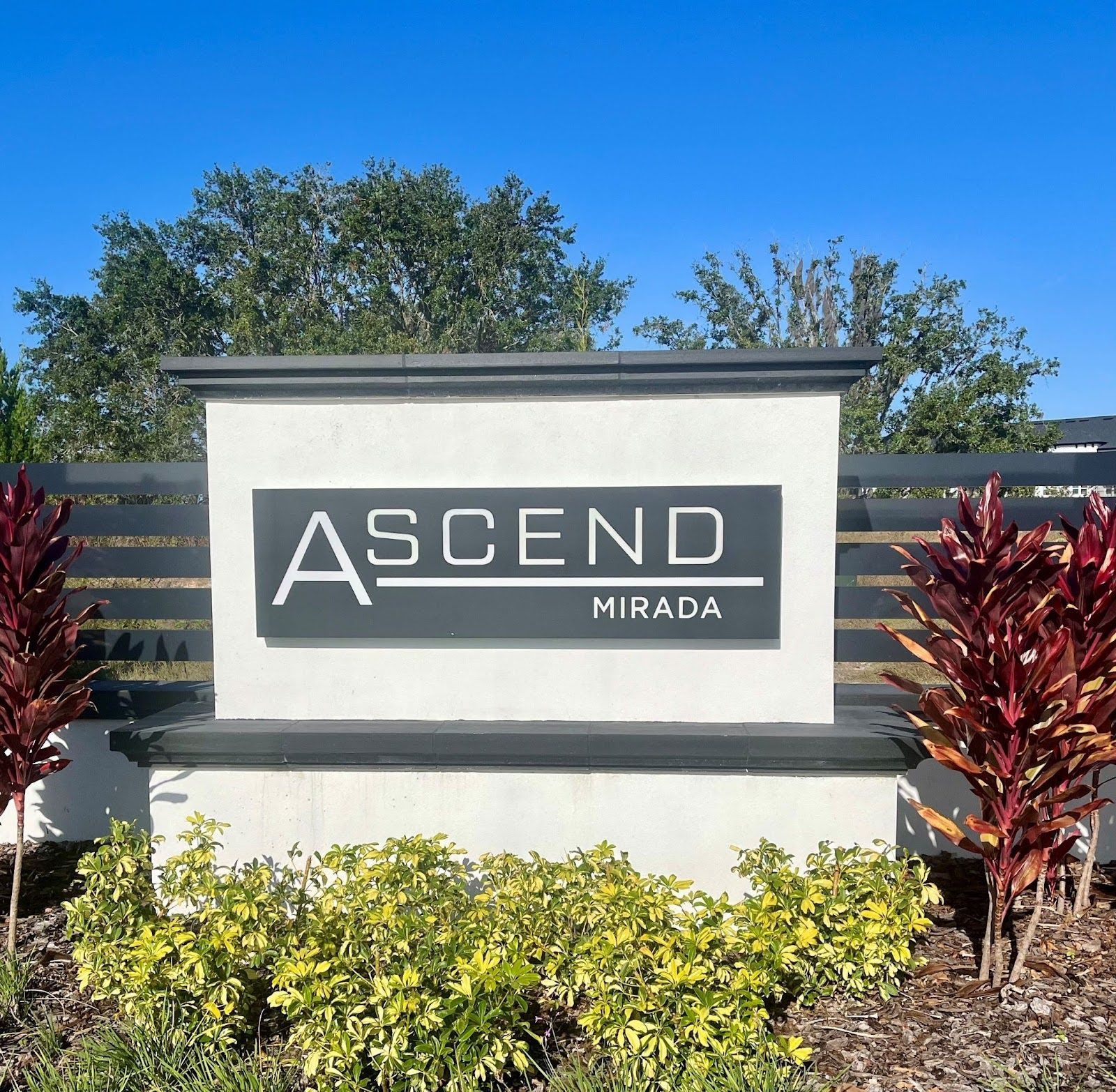 Ascend Mirada sign on a landscaped wall with blue sky and red shrubs