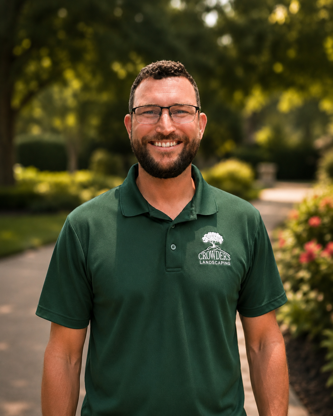 Smiling man in green polo shirt standing outdoors with blurred trees in the background