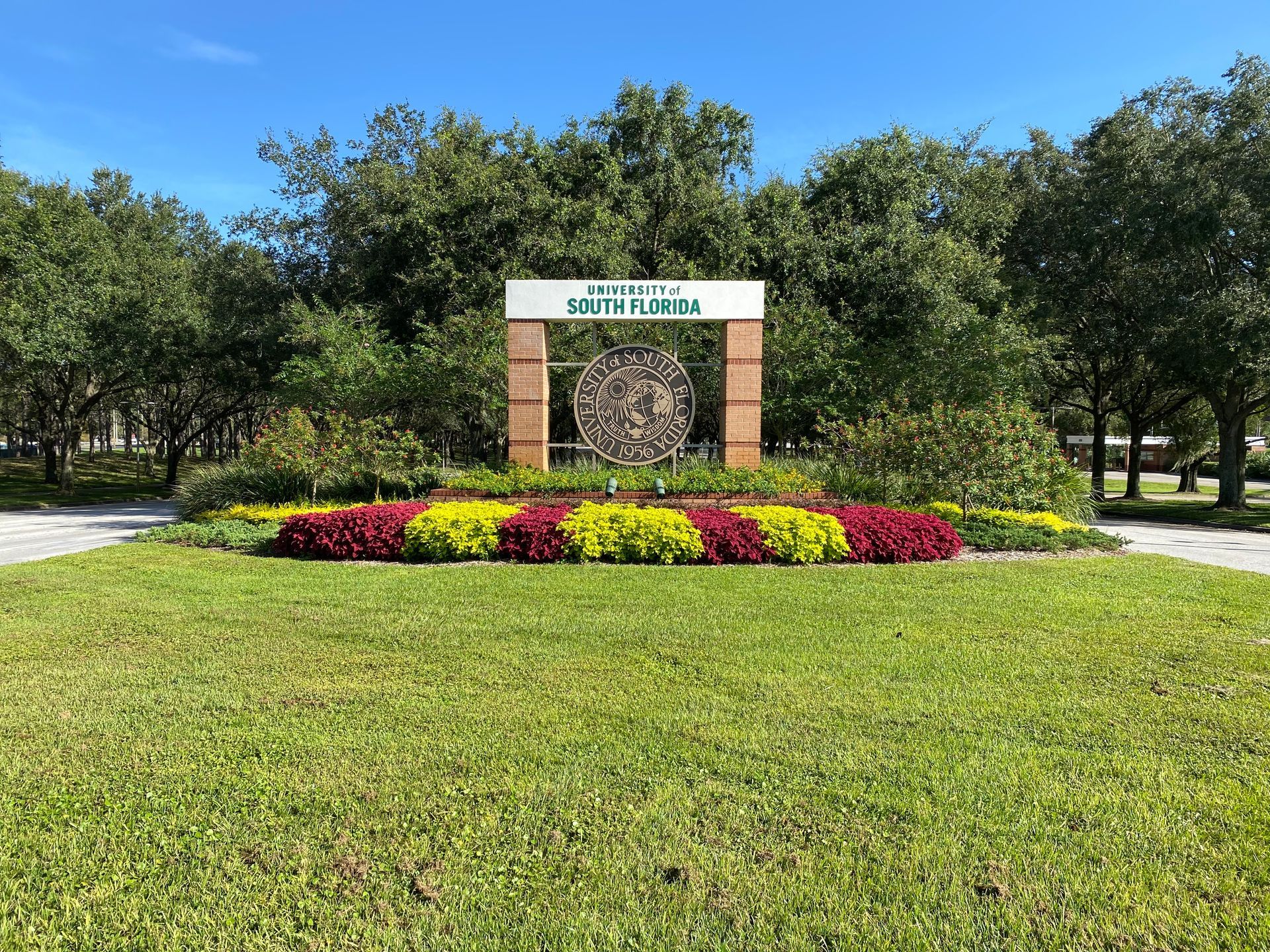 A sign in the middle of a grassy field with flowers and trees in the background.