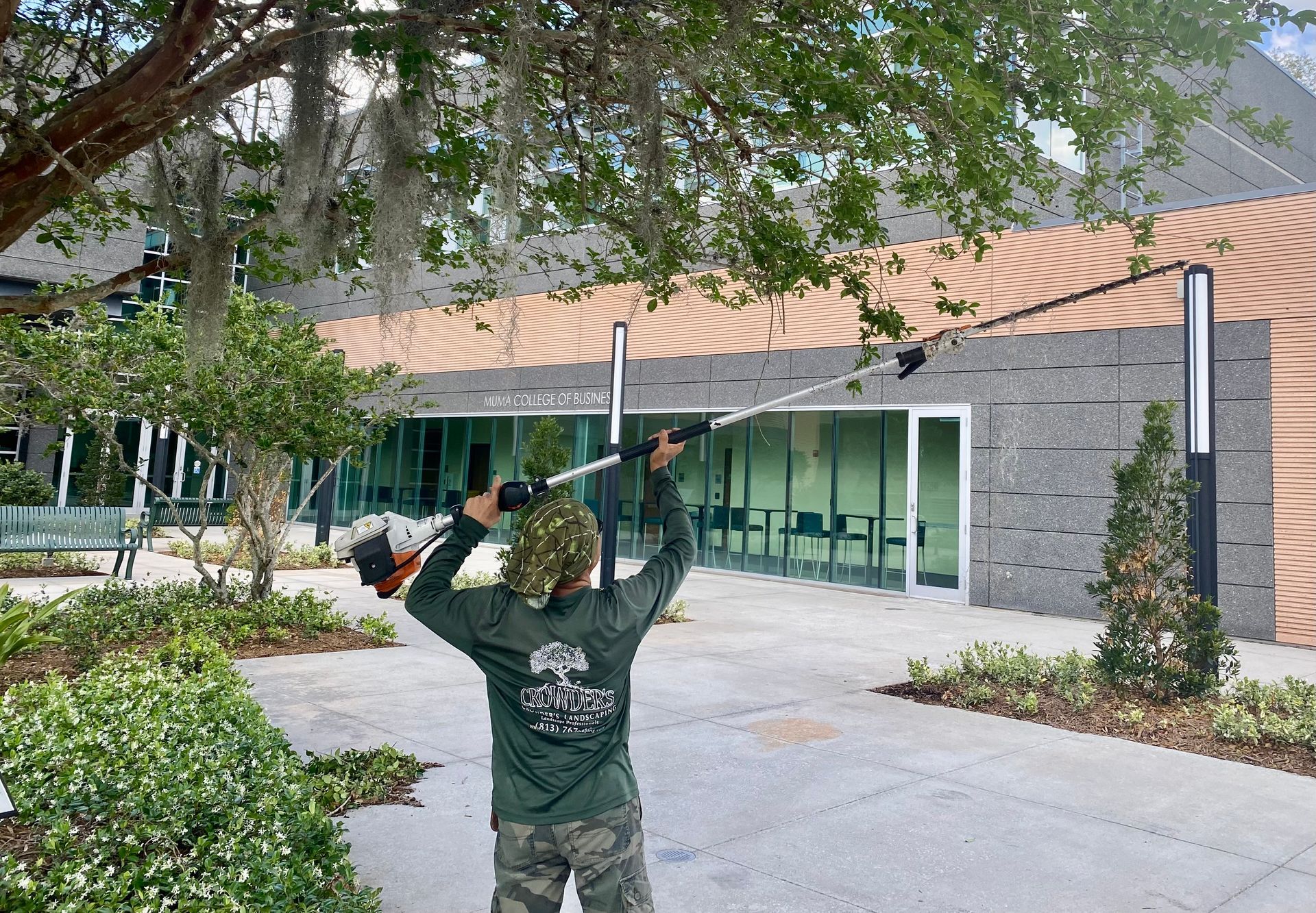 A man is cutting a tree with a lawn mower in front of a building.