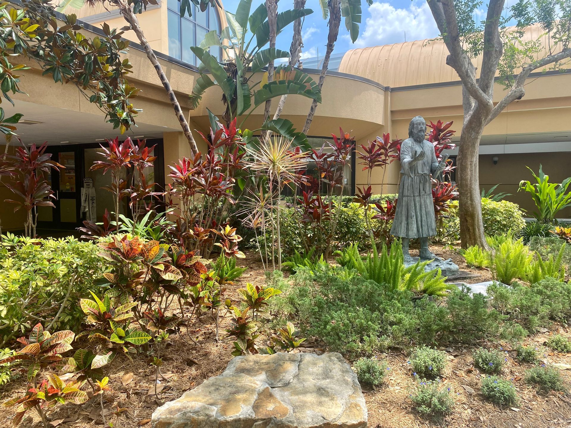 A statue of a woman standing in a garden in front of a building.