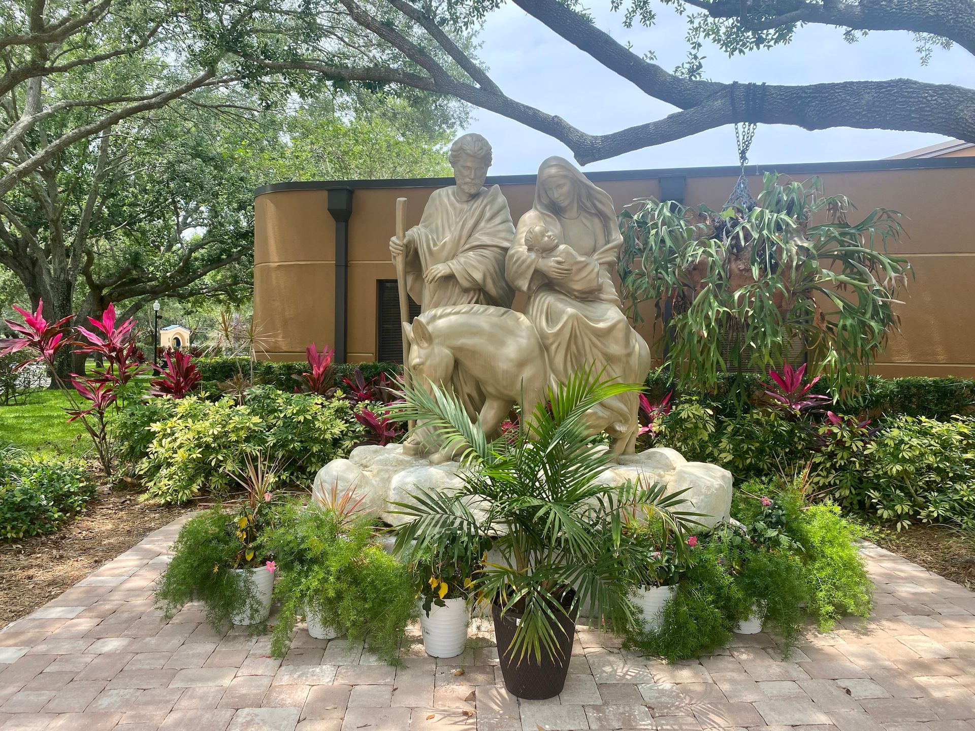 A statue of a man and woman holding a baby is surrounded by potted plants.