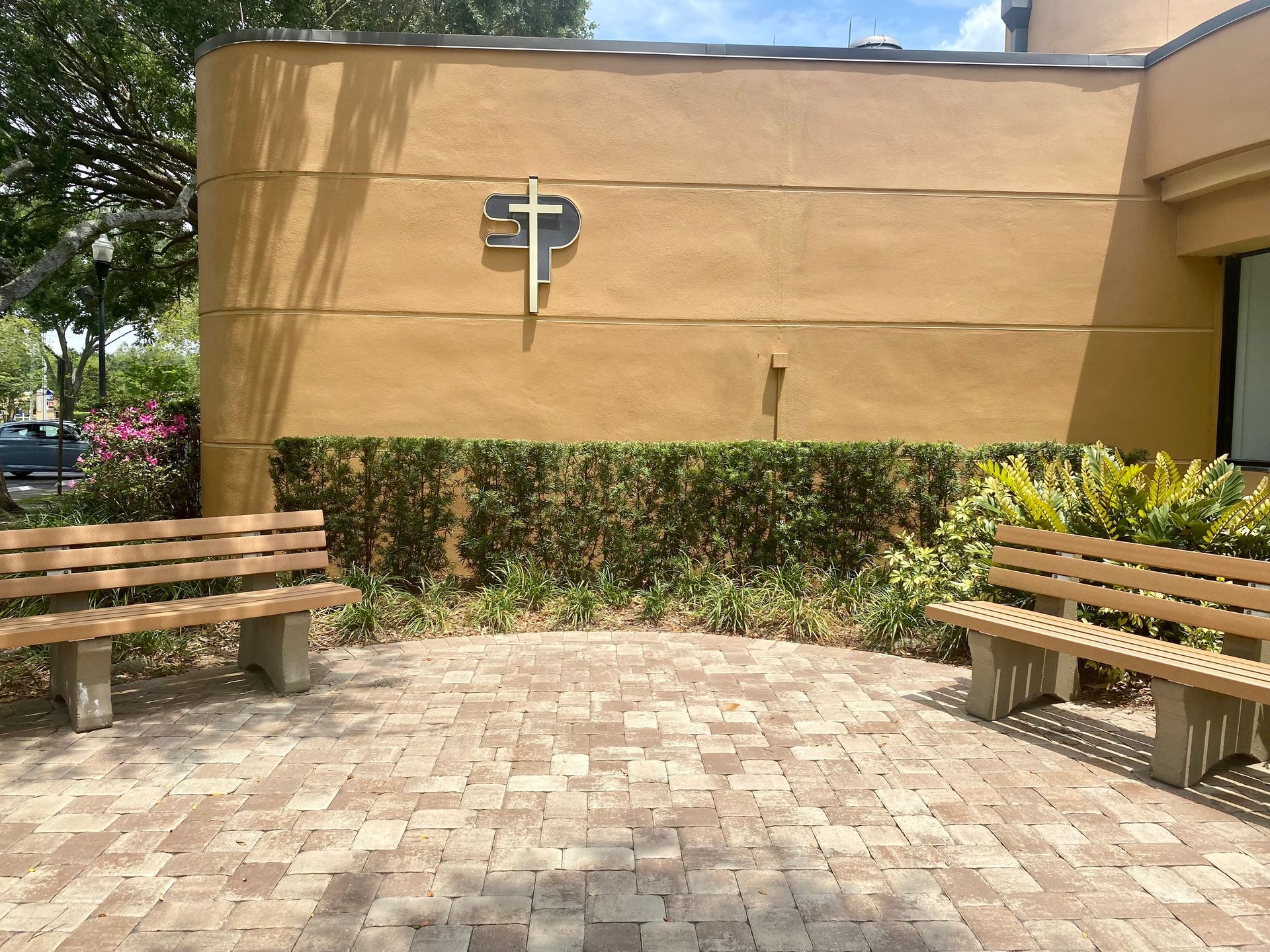Two wooden benches are in front of a building with a cross on the wall.