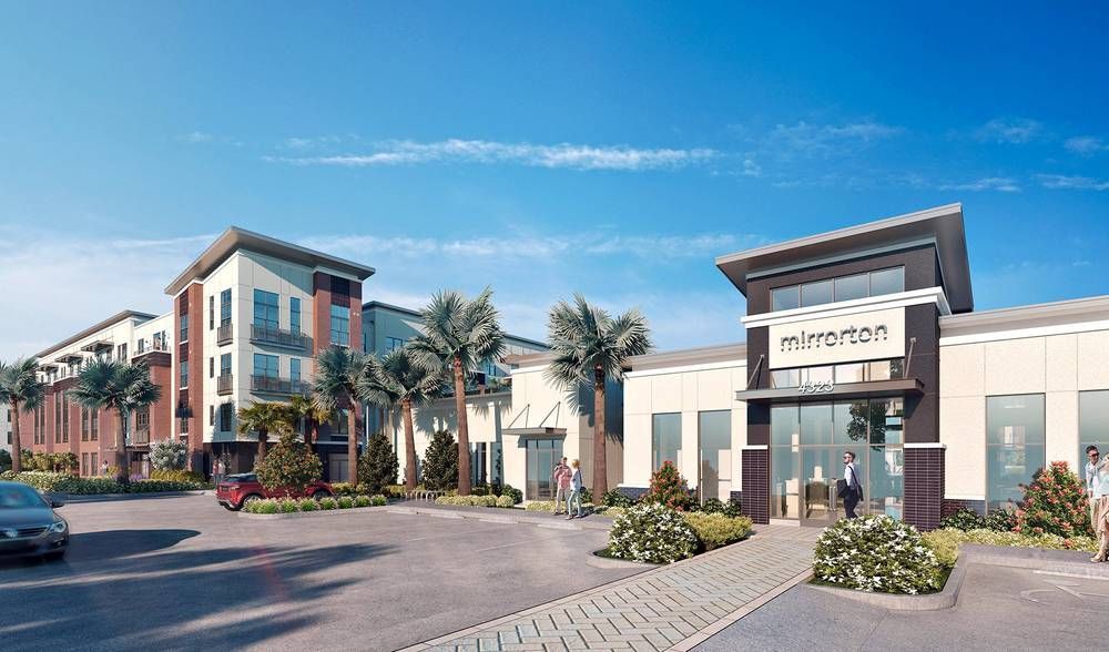 Modern apartment complex with a landscaped entrance and palm trees under a blue sky