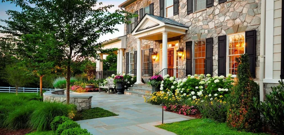 A large stone house with a lush green lawn and flowers in front of it.