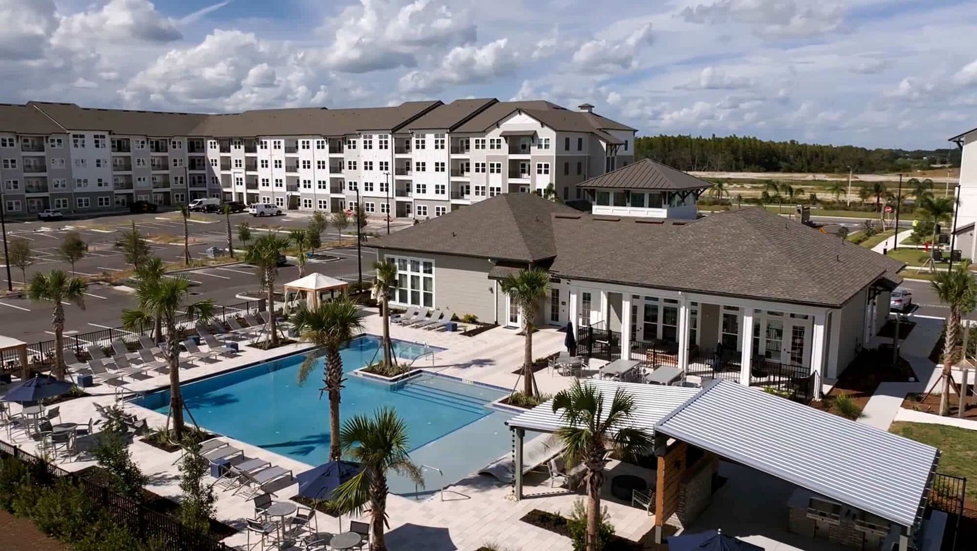 Resort pool courtyard with palm trees and apartment-style buildings under a partly cloudy sky