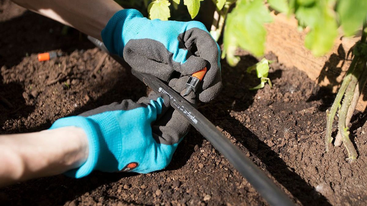 A person wearing gloves is holding a hose in the dirt.- Crowders Landscaping
