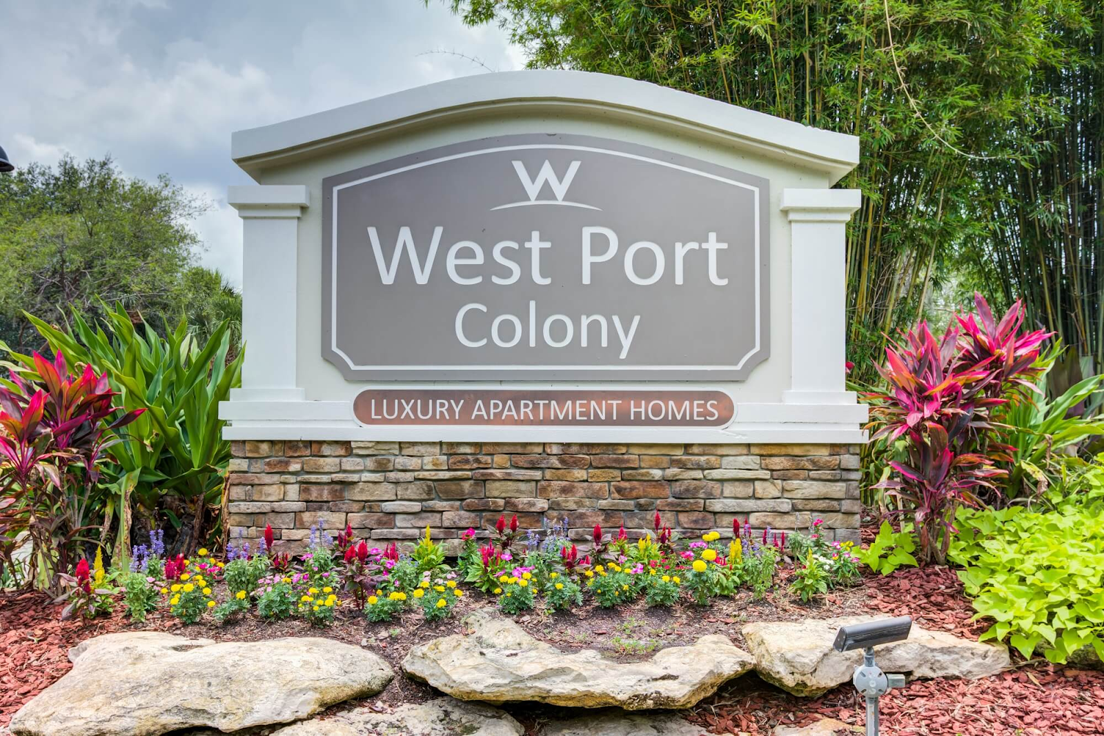 West Port Colony entrance sign with flowers, stone landscaping, and palm trees