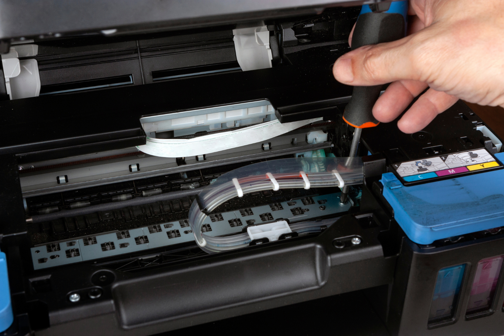 Hand cleaning printer rollers with a tool beside cyan ink cartridges inside an open inkjet printer