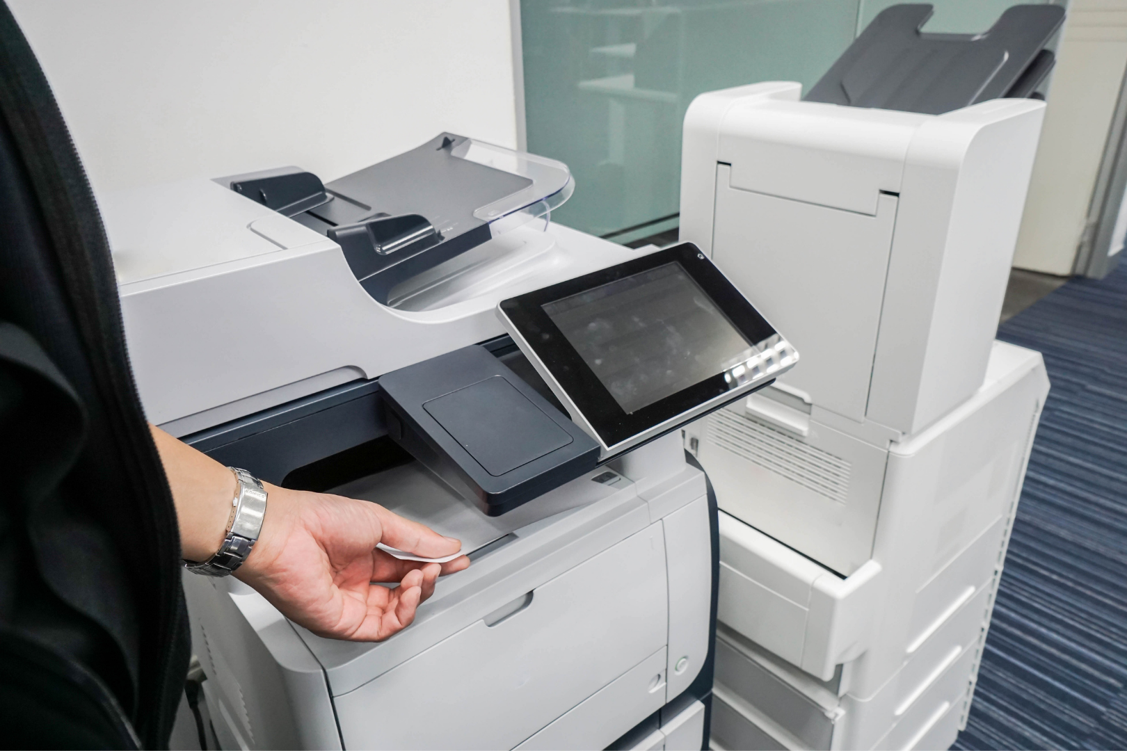 Hand placing paper into a white office copier with a touchscreen control panel