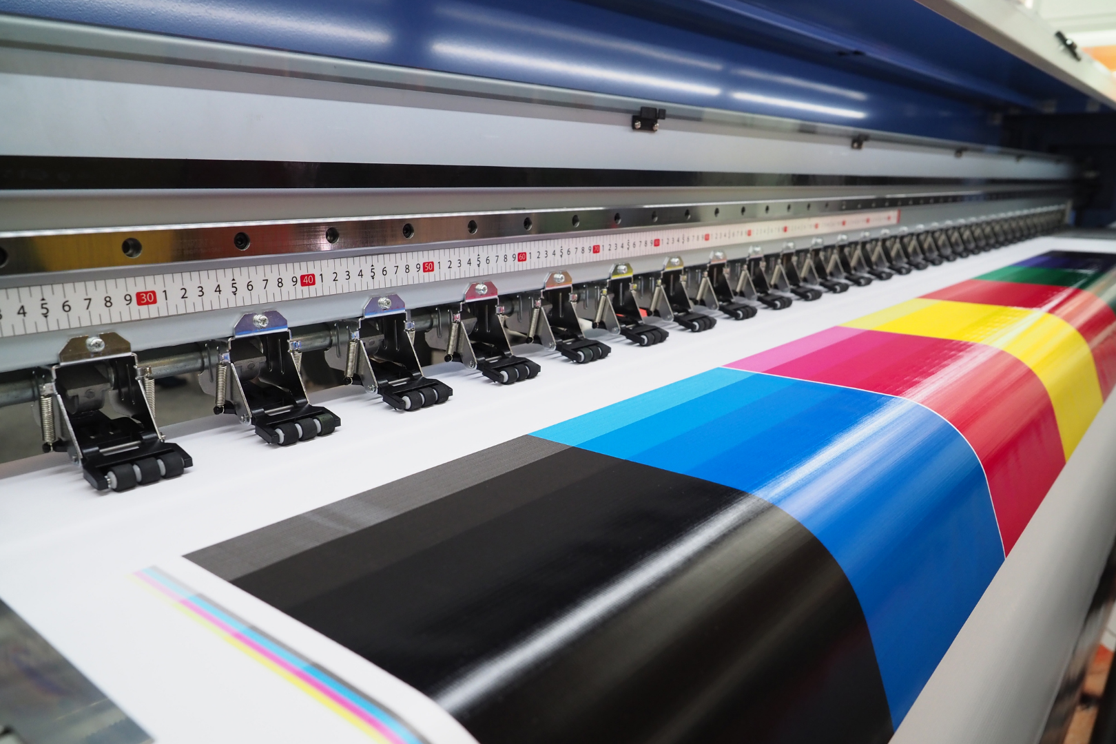 Large-format printer printing CMYK color bands on glossy paper