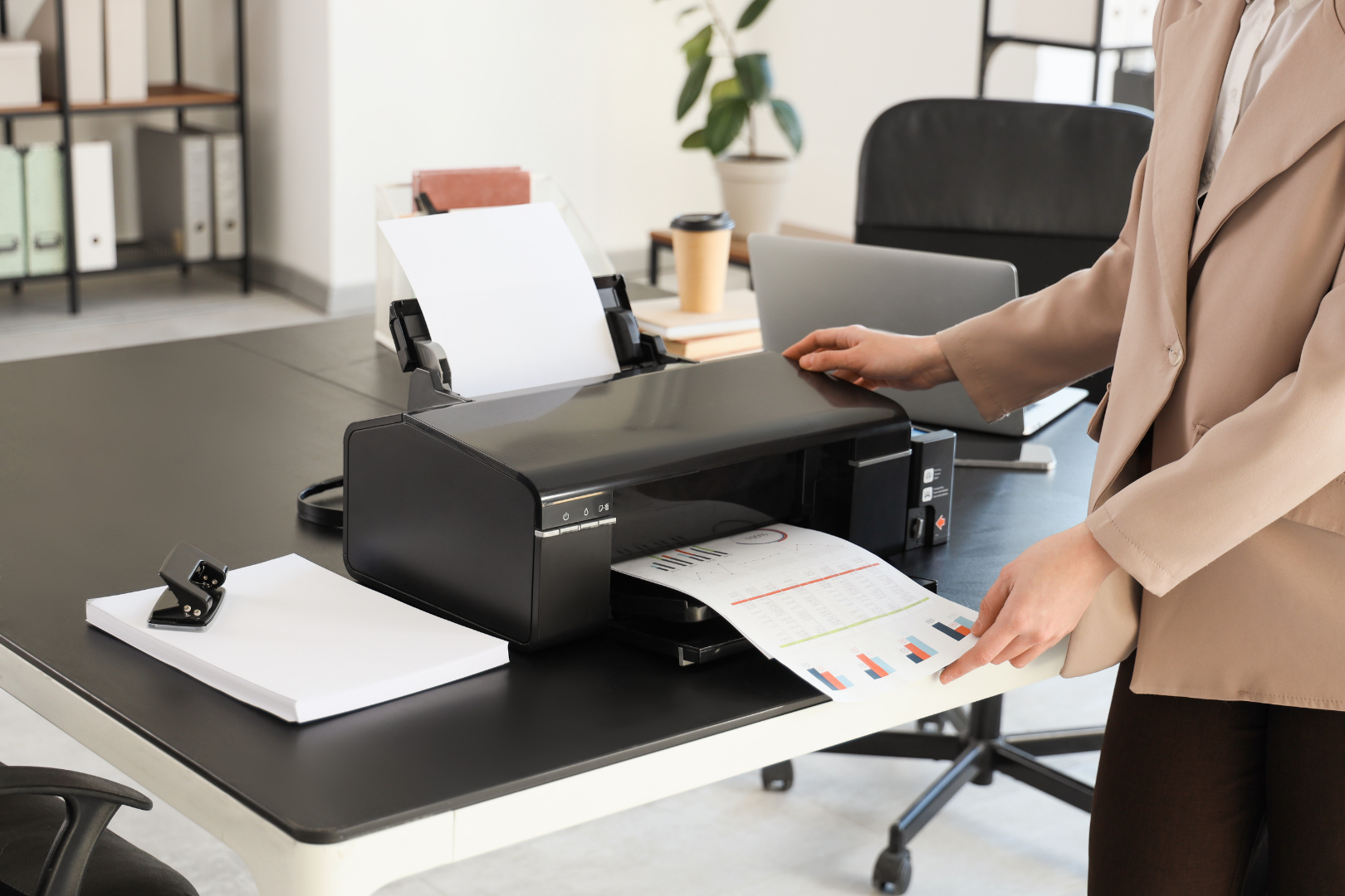Person operating a black office printer to print a color document in a modern workspace