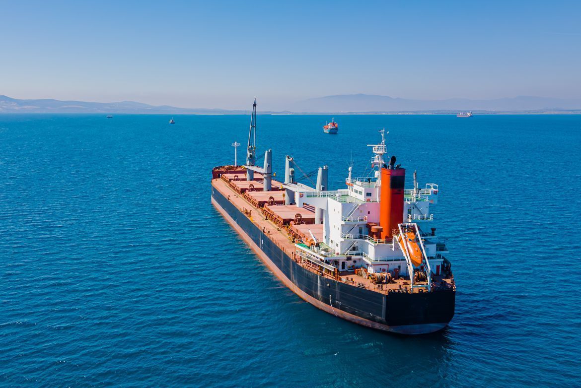 Cargo ship on blue water, with a black hull, white superstructure, and orange smokestack, under a blue sky.