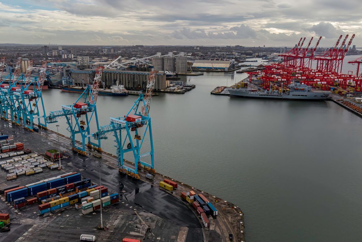 A harbor with container cranes and docked ships. Red and blue cranes, cloudy sky, industrial setting.