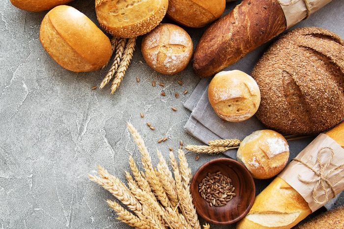 Various fresh baked breads, rolls, and wheat stalks arranged on a grey surface.