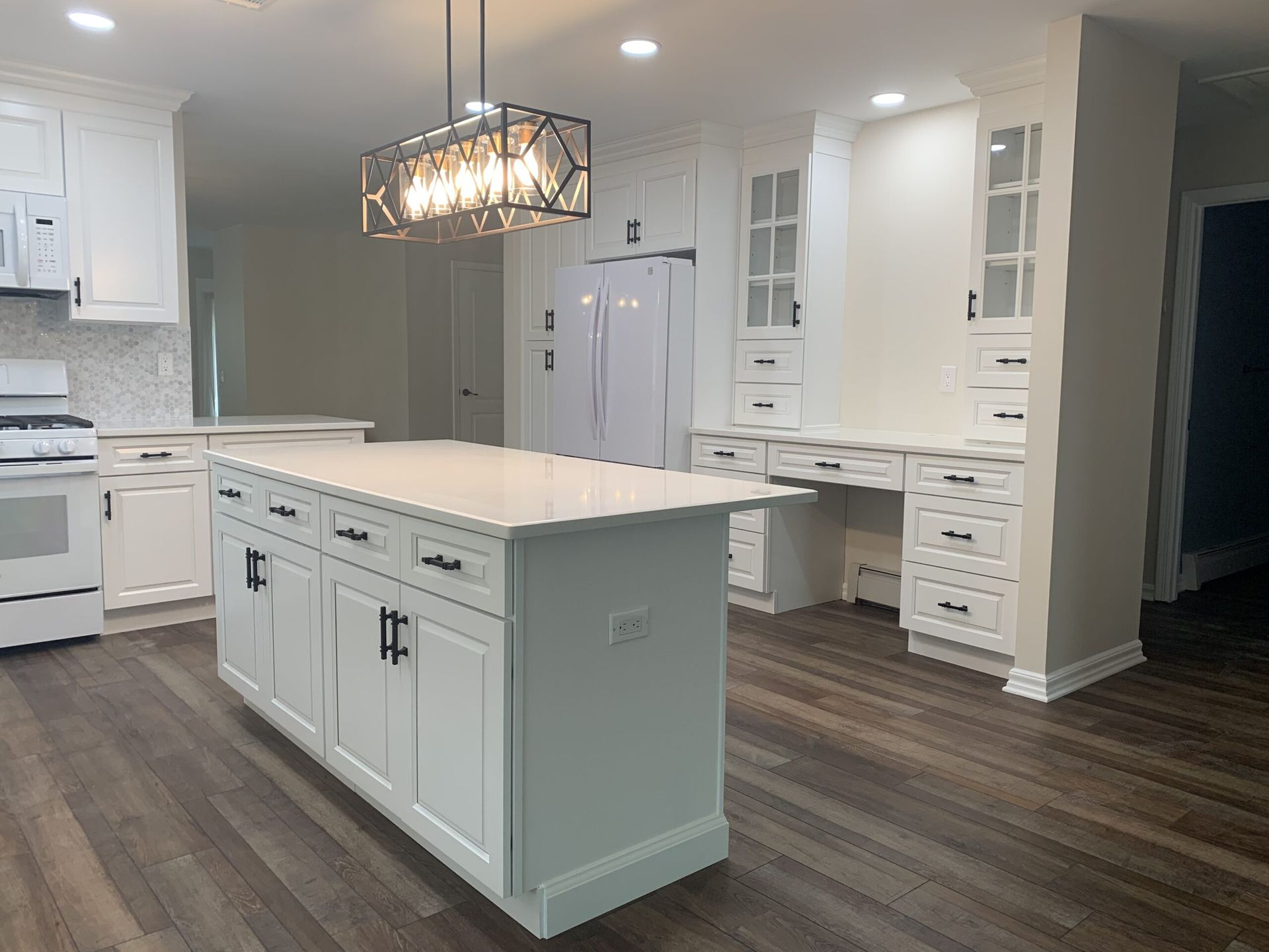Bright modern kitchen with white cabinets, island, pendant light, and dark wood floors