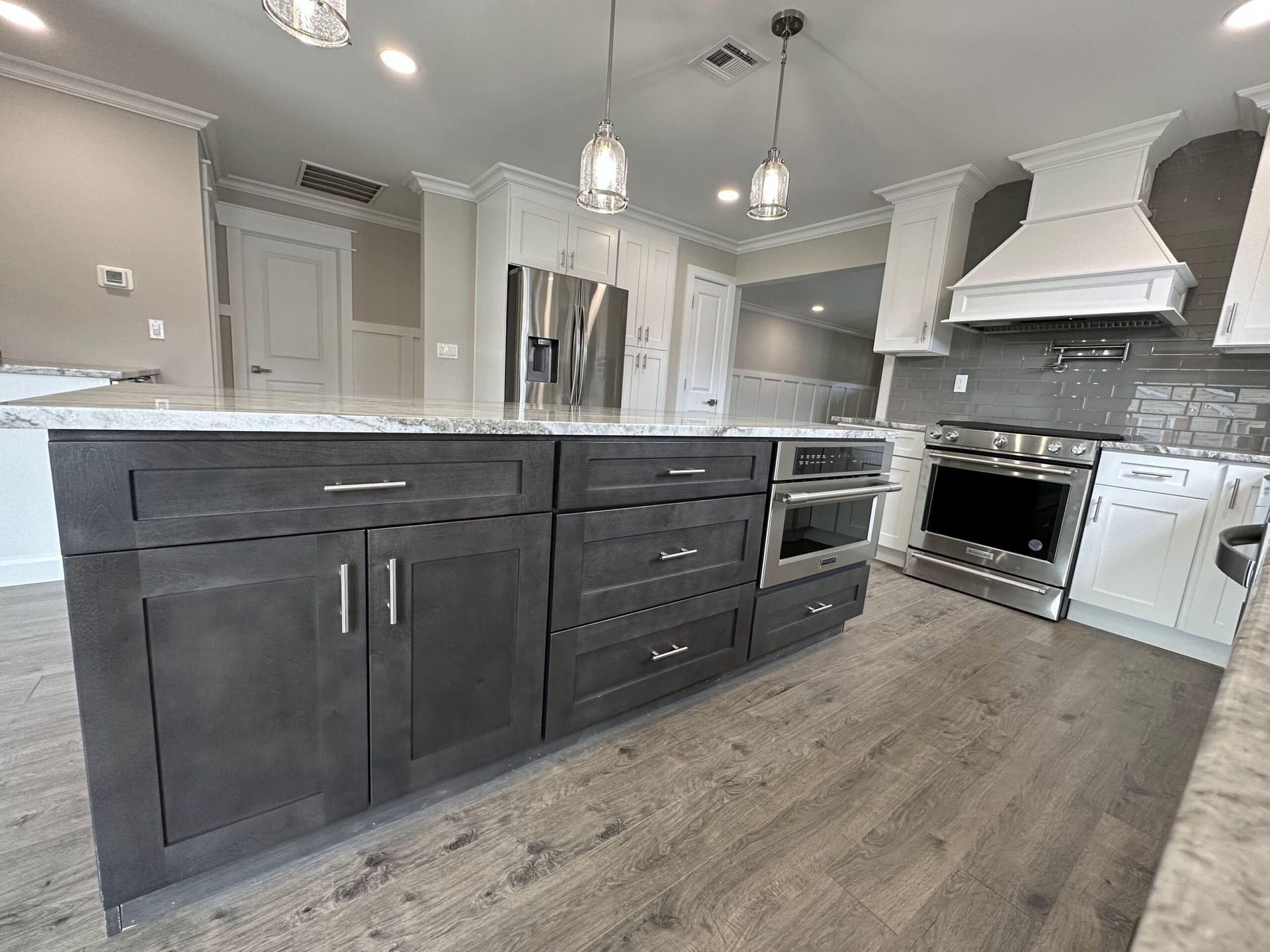Modern white and gray kitchen with island, stainless appliances, pendant lights, and wood-look flooring