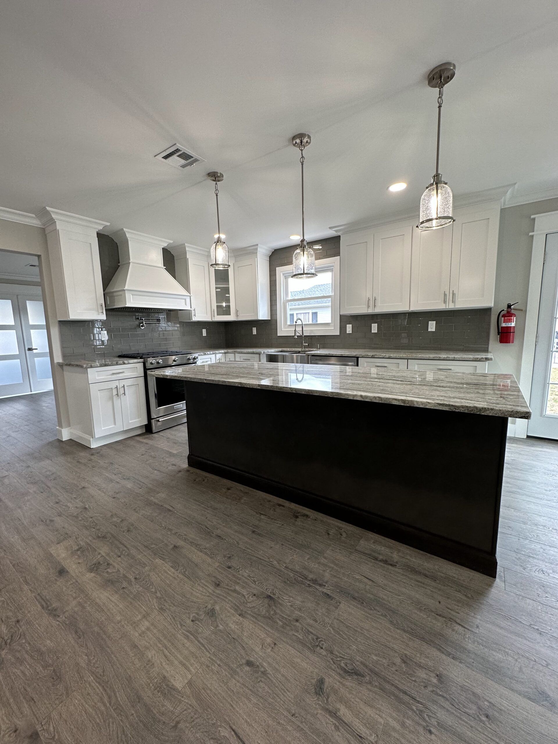 Bright modern kitchen with white cabinets, dark island, gray tile backsplash, and pendant lights