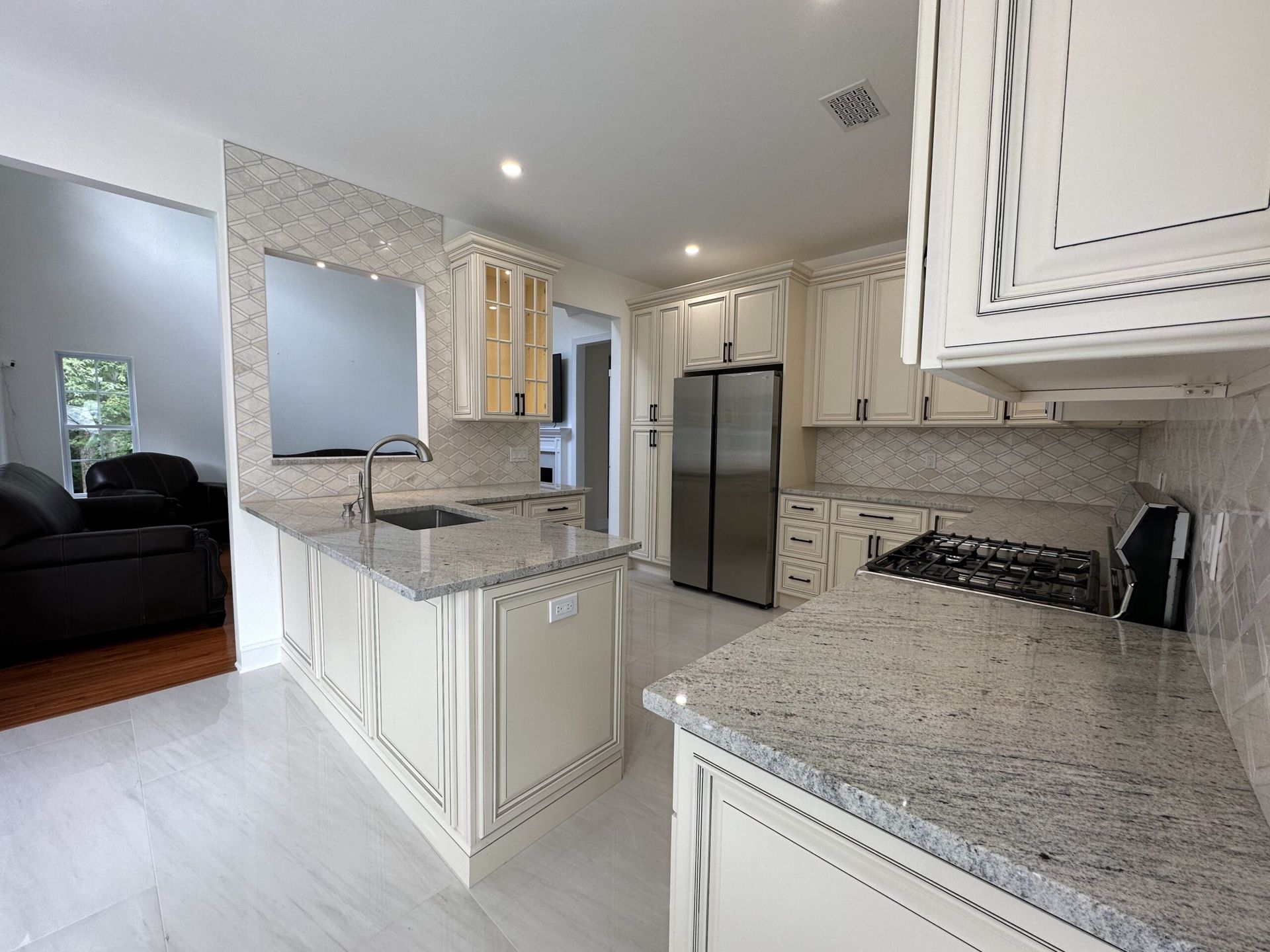 Bright modern kitchen with granite countertops, white cabinets, stainless steel fridge, and a sink island.
