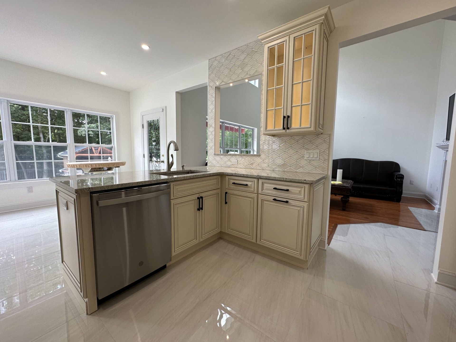 Bright kitchen with beige cabinets, tiled backsplash, island, and glossy white floor, opening to a living room