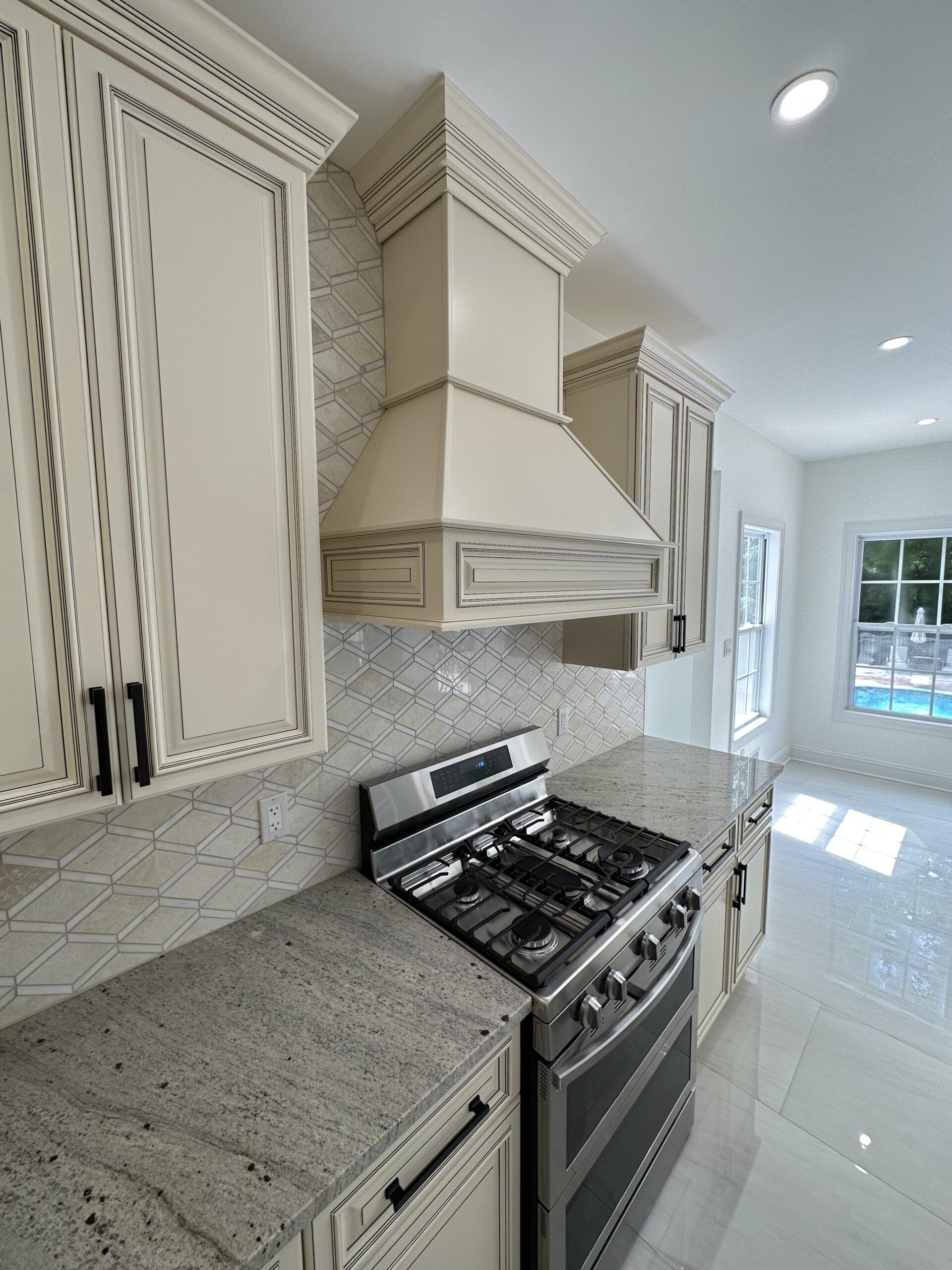 Bright modern kitchen with white cabinets, granite countertop, gas range, and patterned tile backsplash