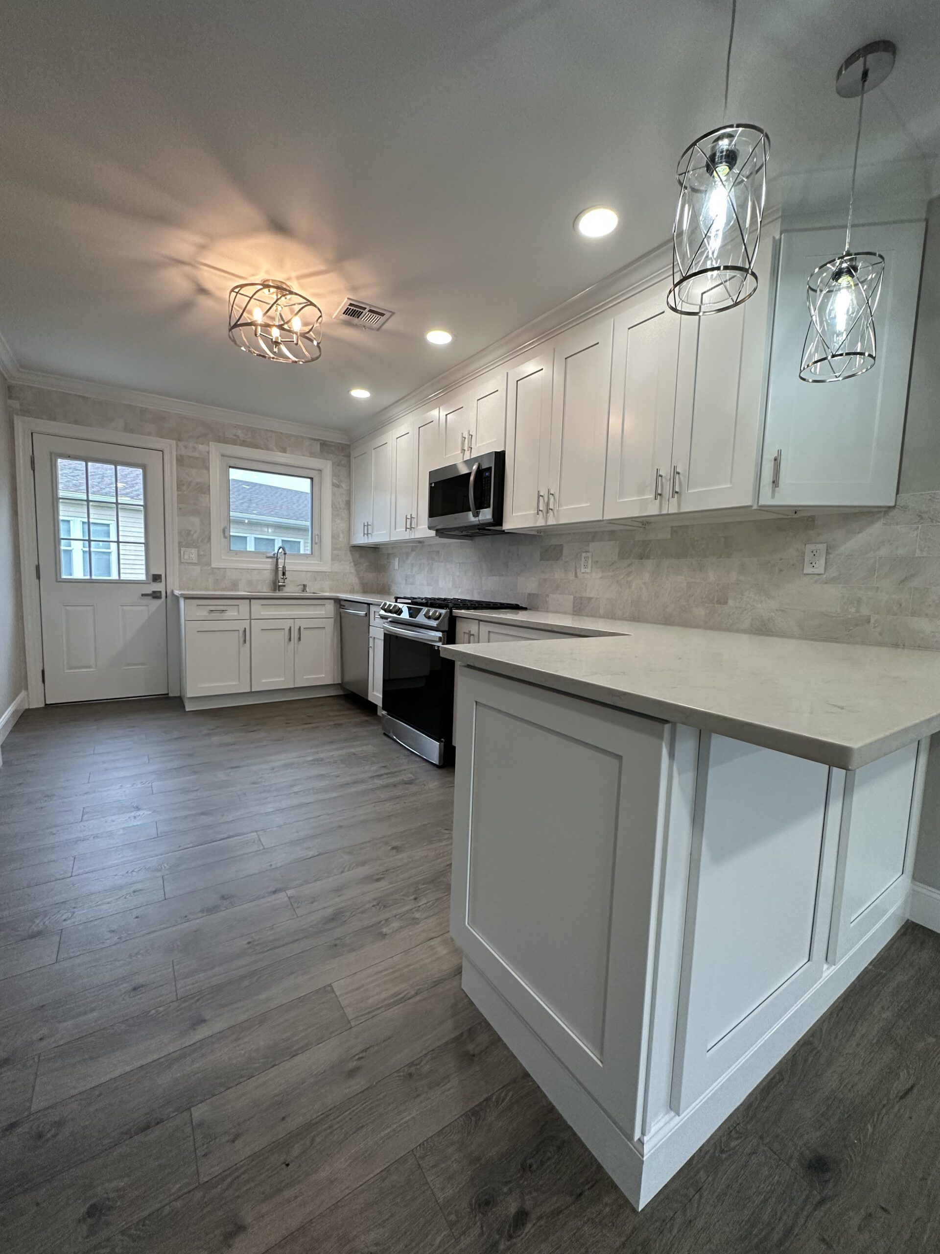 Bright white modern kitchen with island, pendant lights, stainless appliances, and wood-look flooring