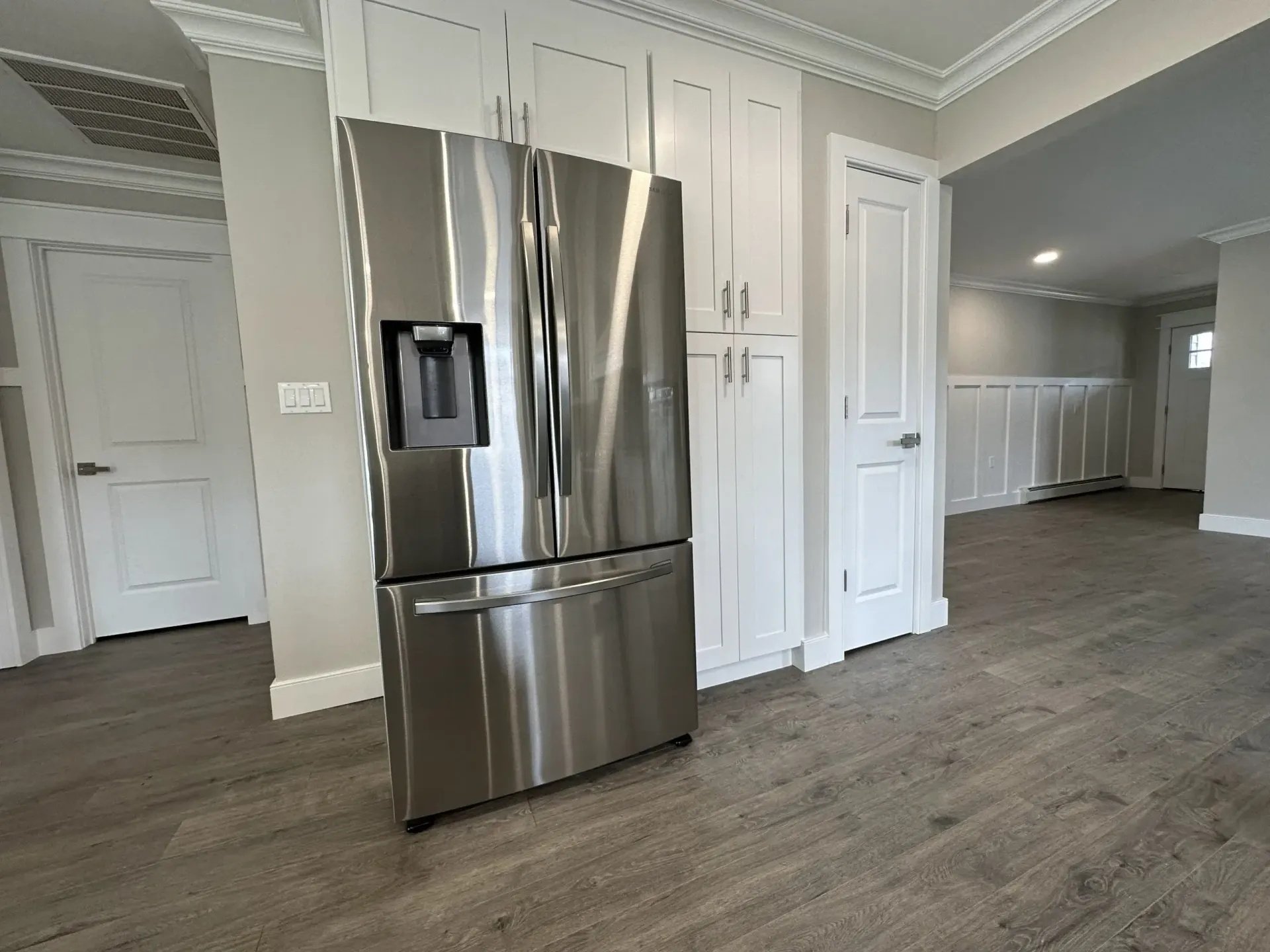 Modern kitchen with stainless steel refrigerator and white cabinets on wood floors