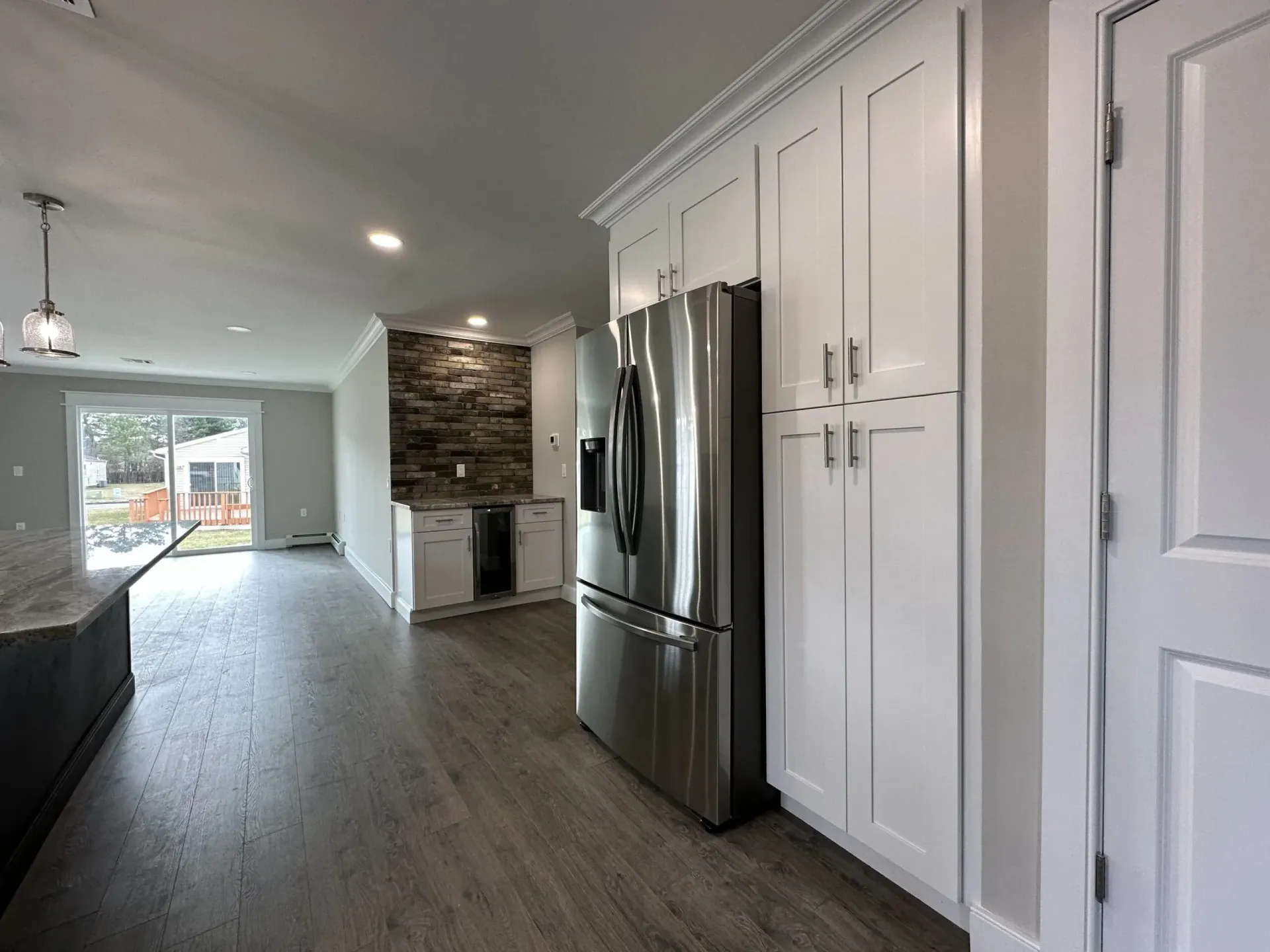 Bright modern kitchen with stainless steel fridge, white cabinets, stone backsplash, and wood-look flooring