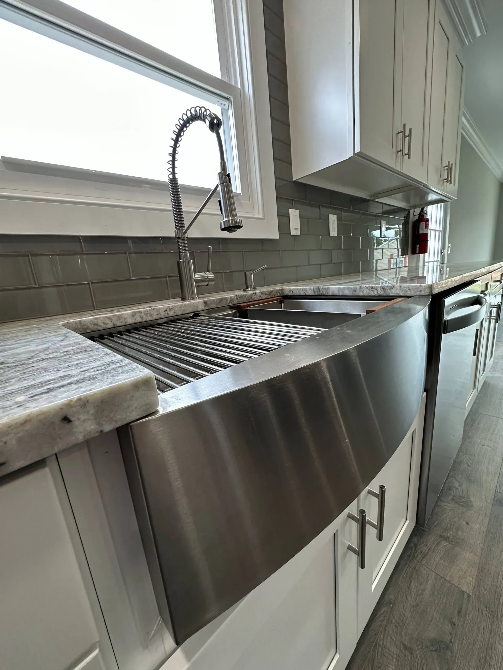 Stainless steel kitchen sink under a window with a high-arc faucet and drying rack in a bright modern kitchen