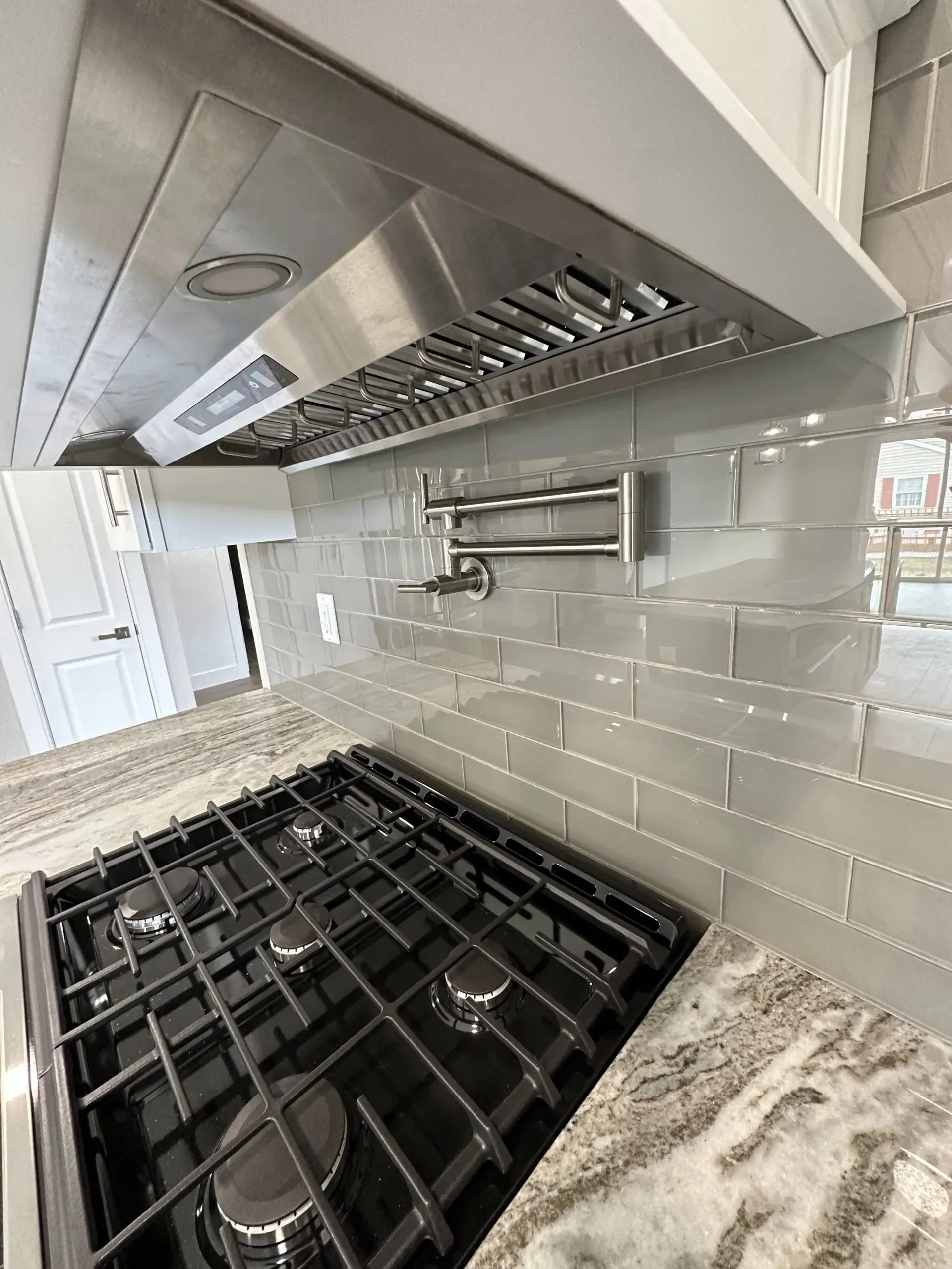 Modern kitchen stove beneath stainless steel range hood, with white subway tile backsplash and granite countertop
