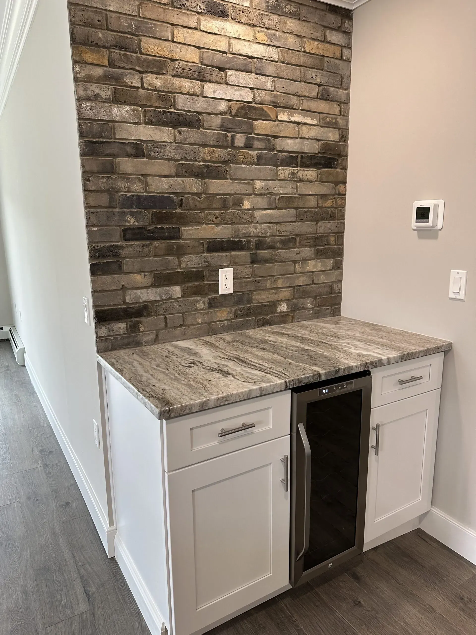 Built-in kitchen wet bar with stone backsplash, granite countertop, and gray cabinets with mini fridge.