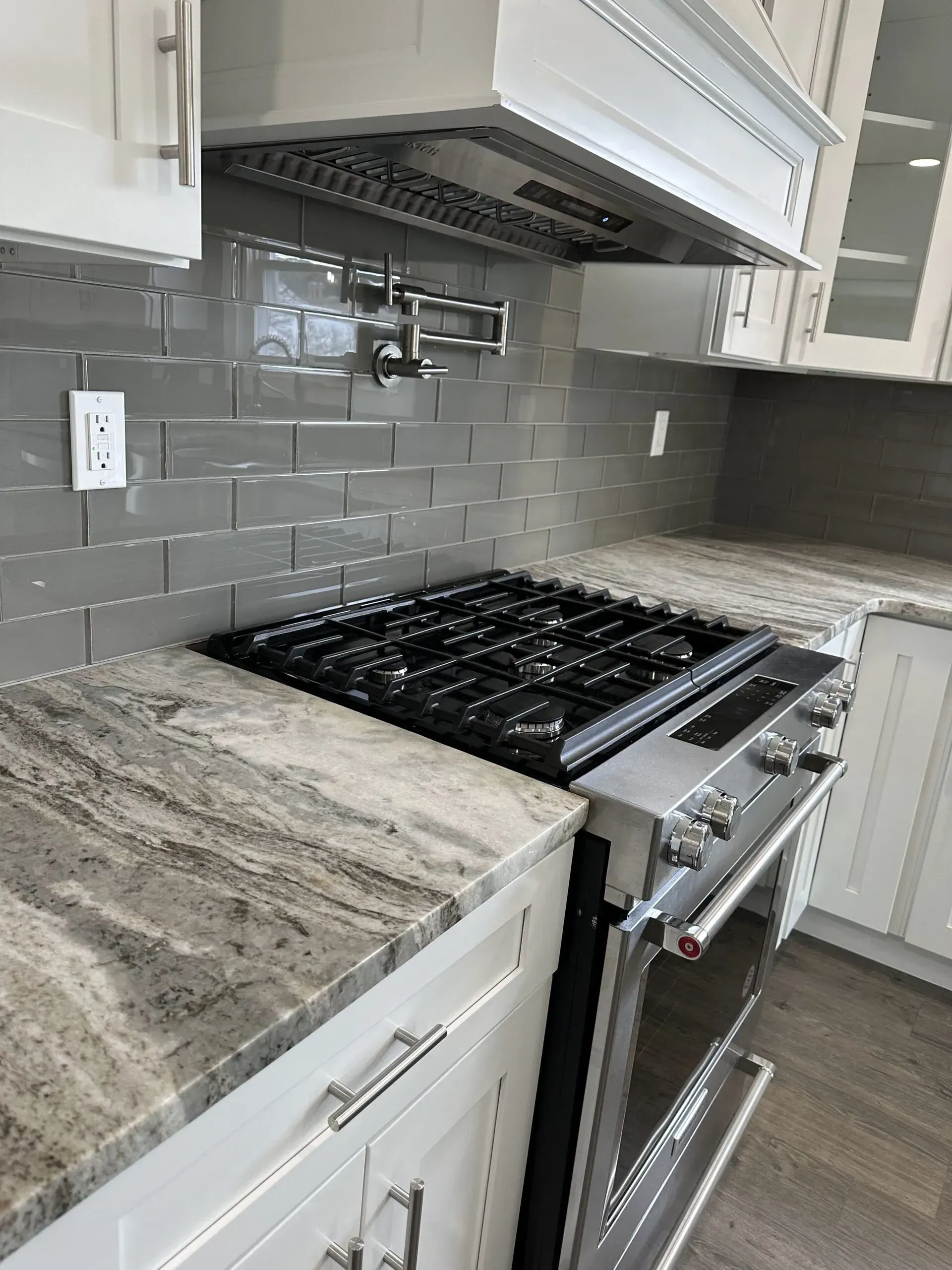 Modern kitchen with white cabinets, gray tile backsplash, granite counter, and stainless gas range under a hood