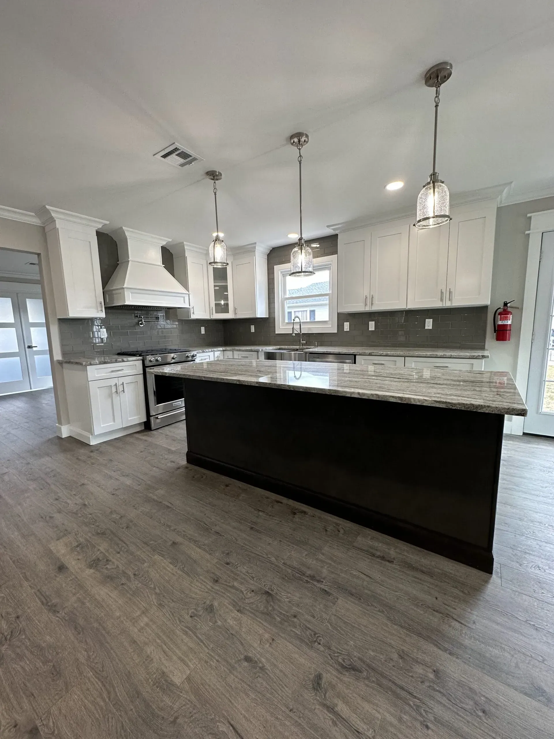 Modern kitchen with gray cabinets, black island, pendant lights, and wood-look flooring