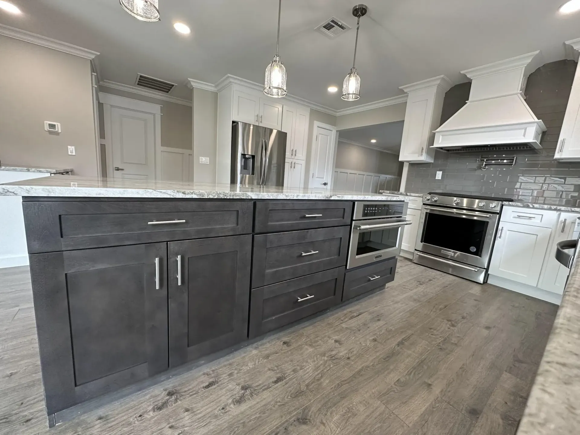 Modern white-and-gray kitchen with dark island cabinets, stainless appliances, and pendant lights.