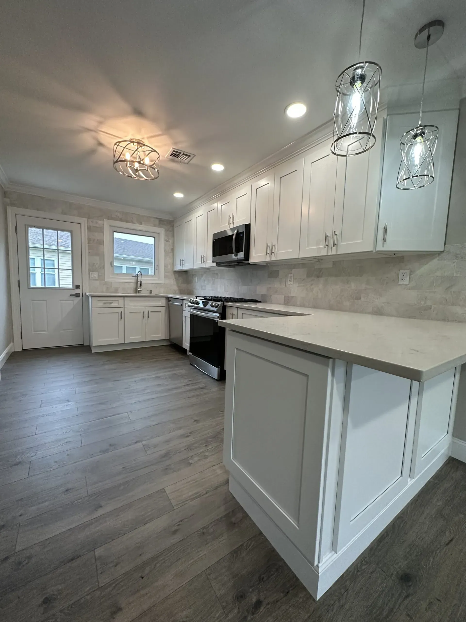 Bright white kitchen with pendant lights, gray island, stainless appliances, and wood-look floors