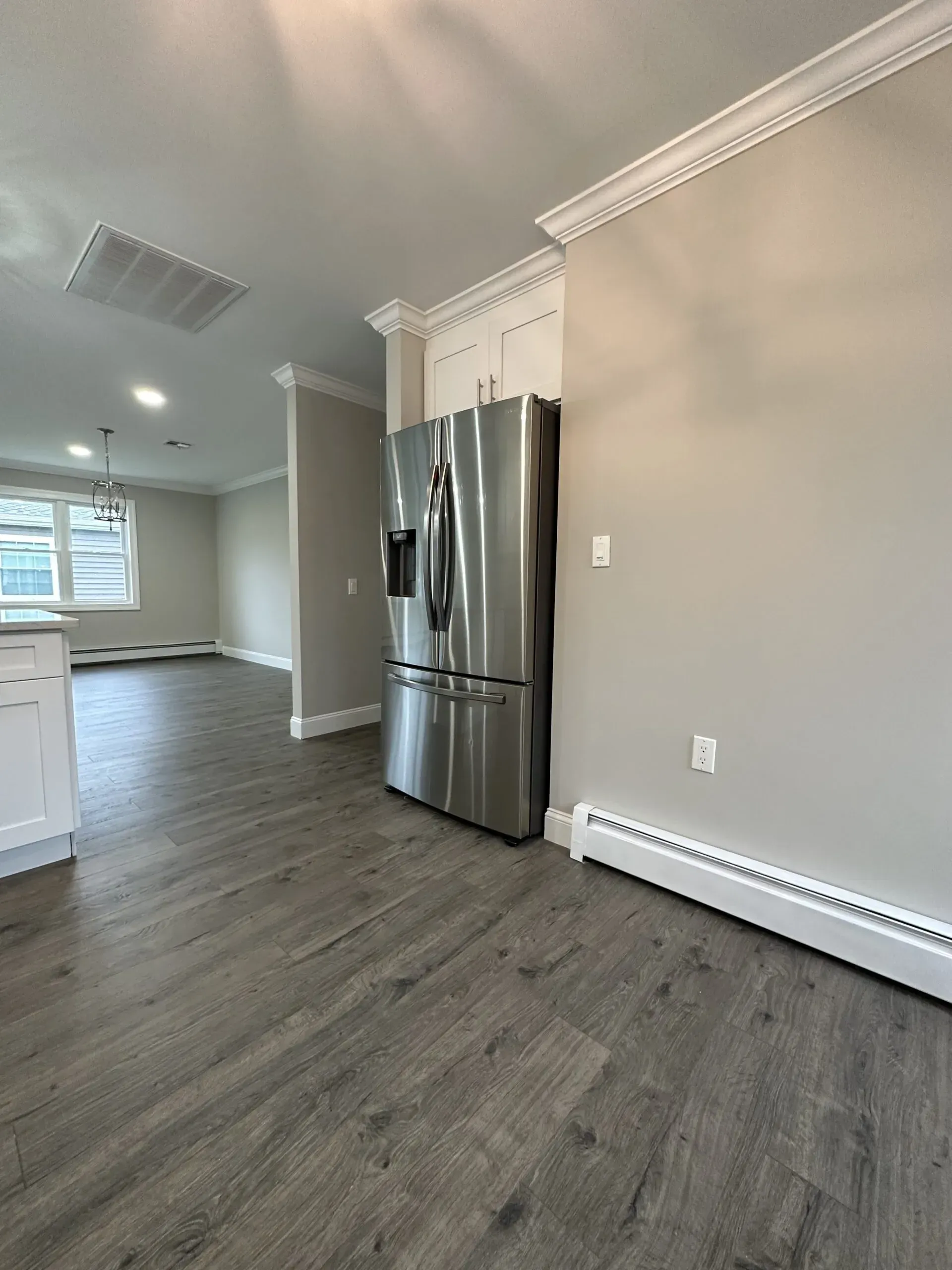 Empty modern kitchen with stainless steel refrigerator, light gray walls, and wood-look flooring.