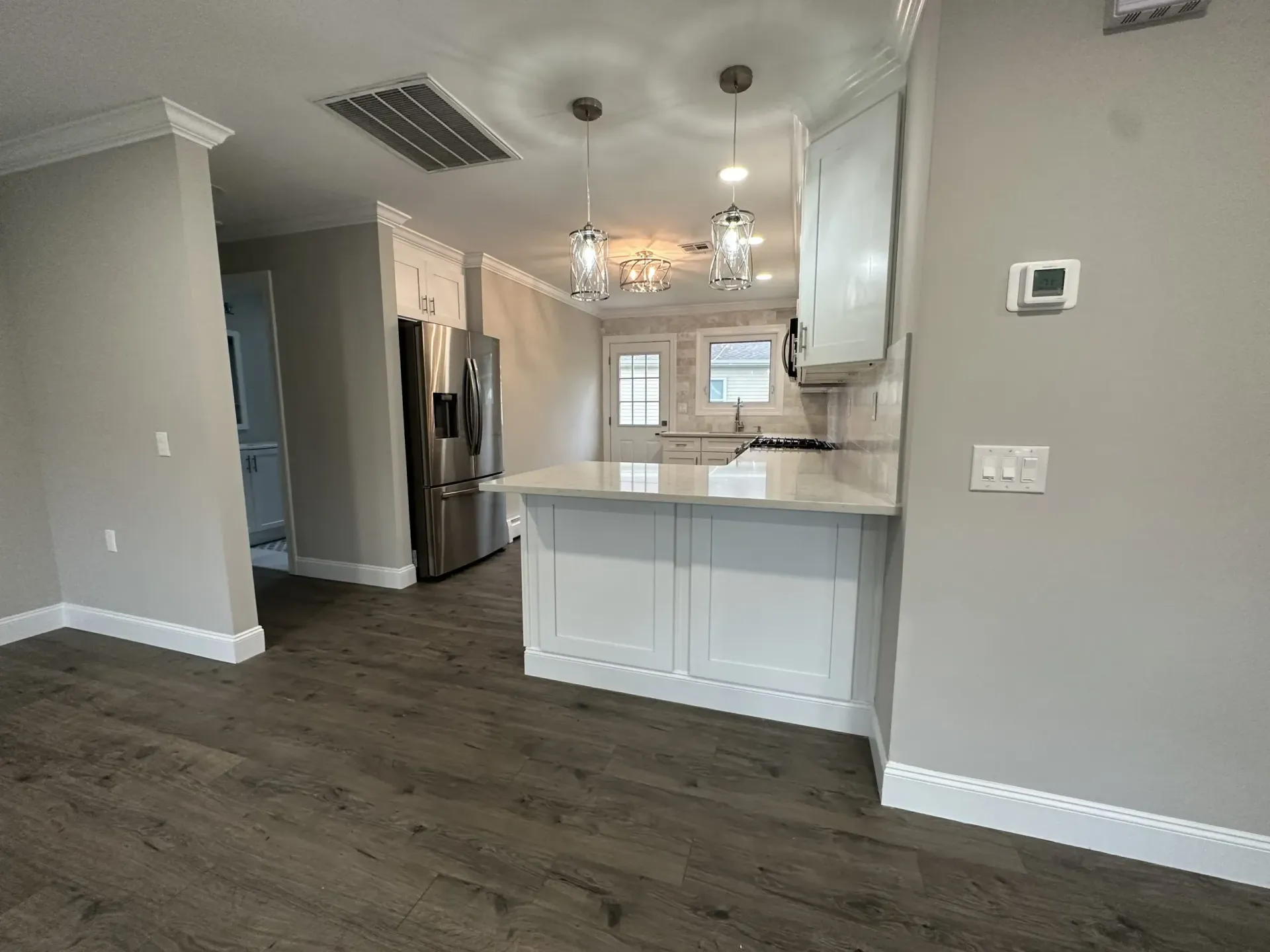 Modern kitchen with white cabinets, stainless fridge, island, and dark wood floors