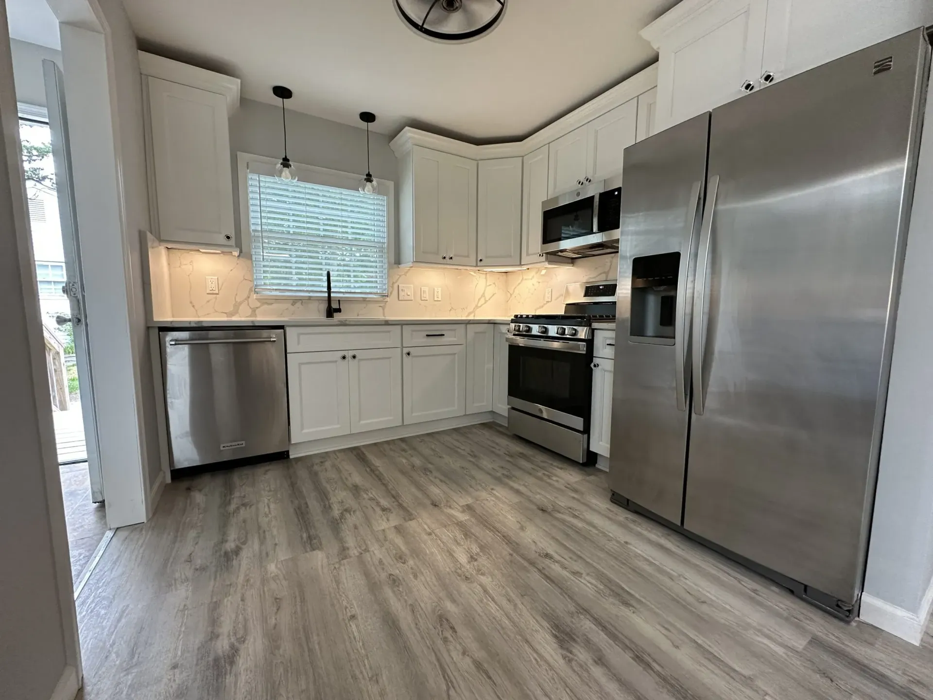 Modern kitchen with white cabinets, stainless steel appliances, and gray wood-look flooring