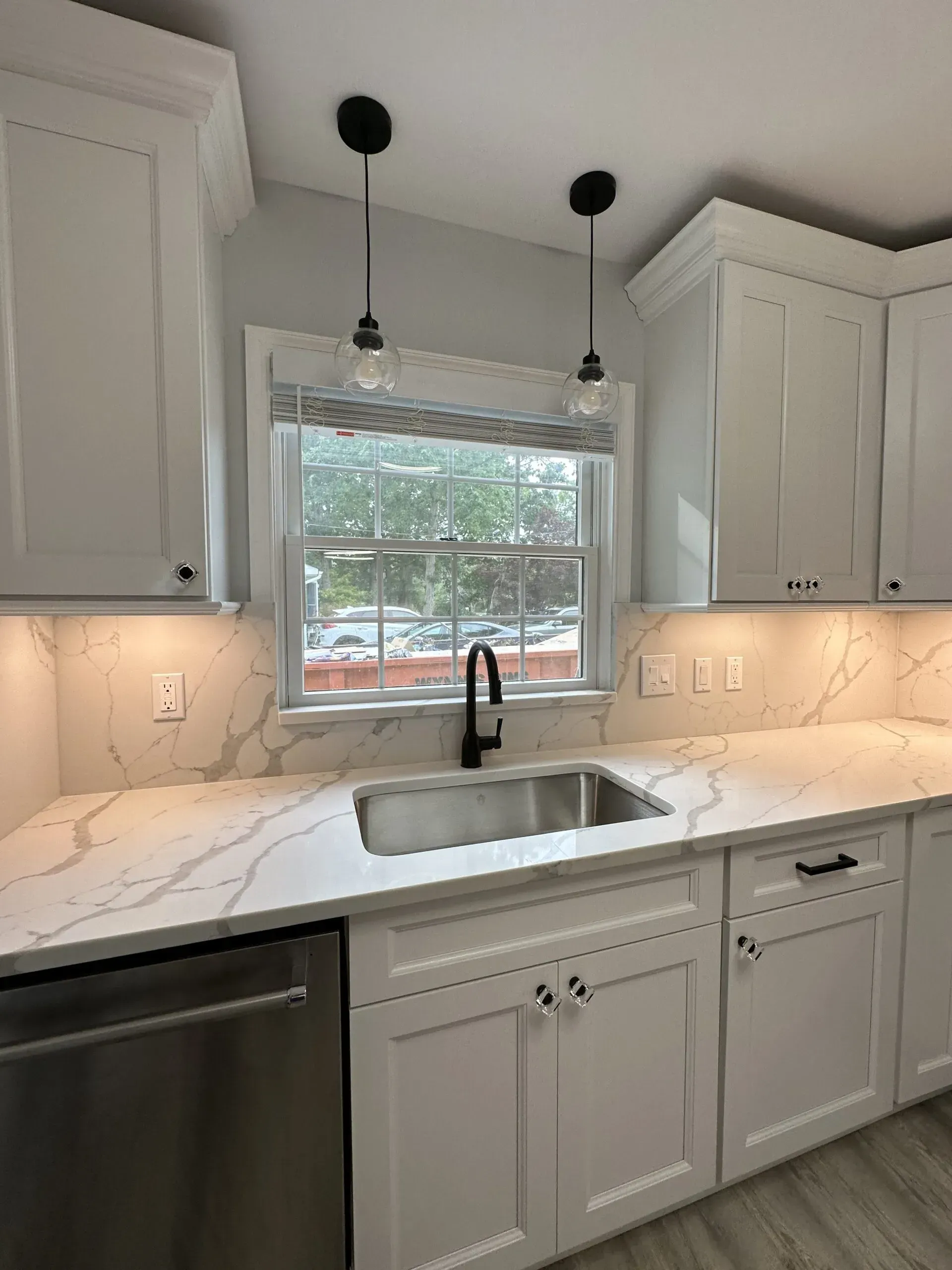 Modern kitchen with white cabinets, marble-look counters, window over sink, and black pendant lights