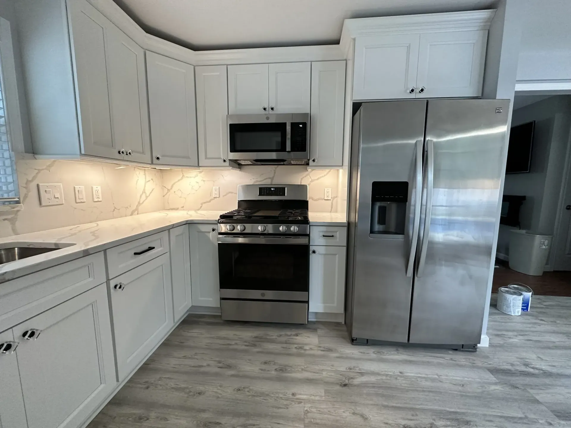 Bright white kitchen with stainless steel appliances, white cabinets, and light wood flooring
