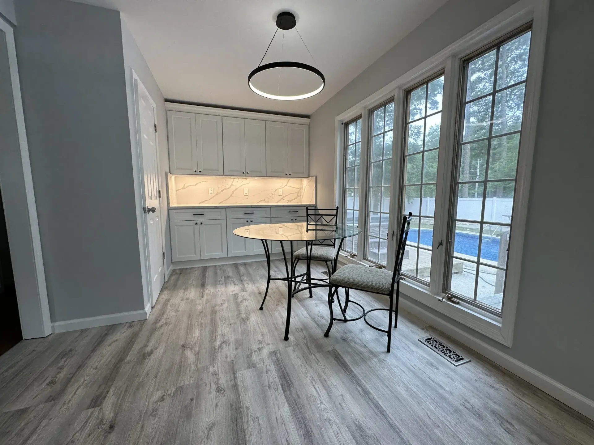 Modern kitchen with white cabinets, wood floors, dining table, and large windows.