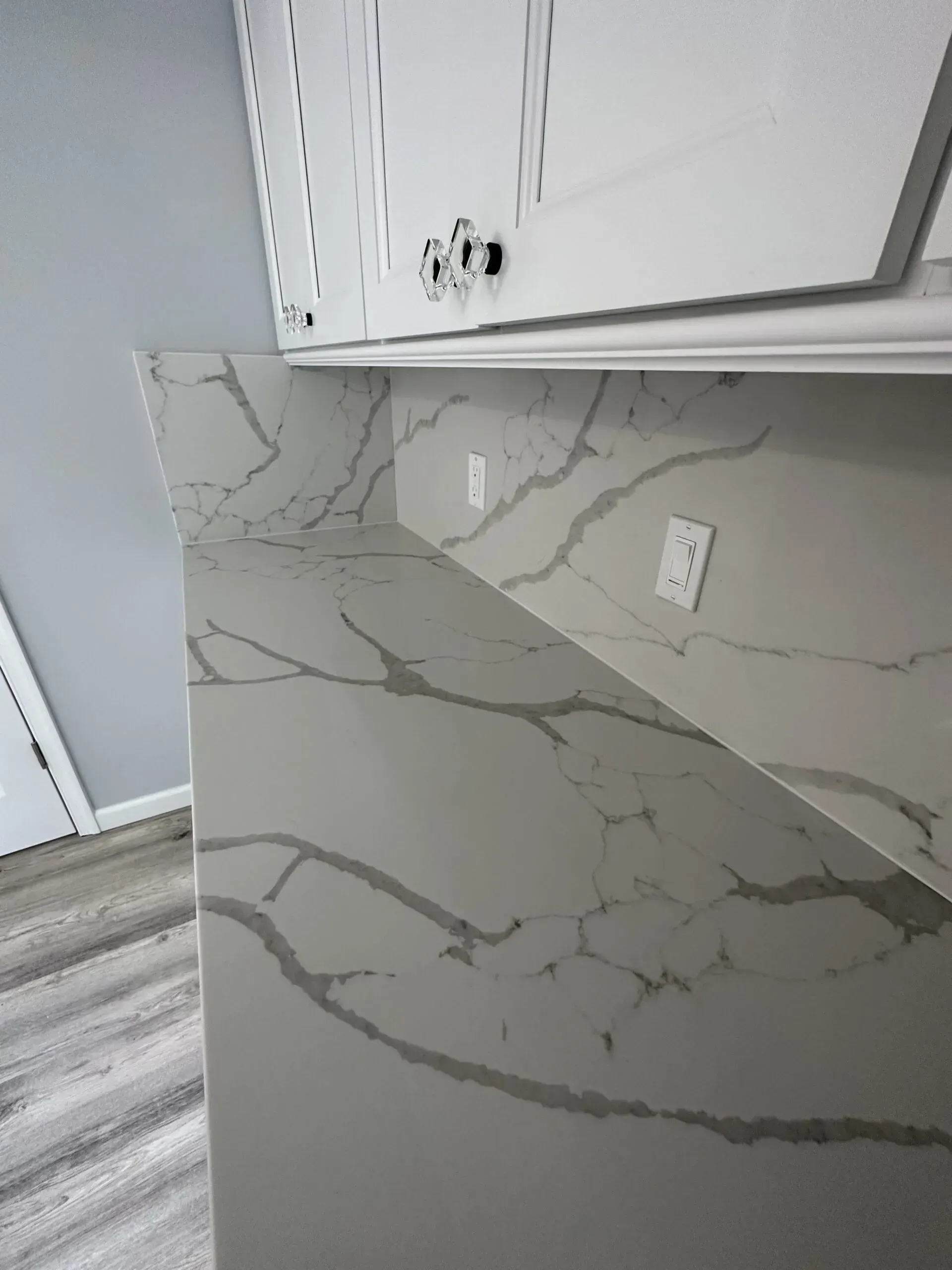 Marble-look kitchen countertop corner with white cabinets and electrical outlets