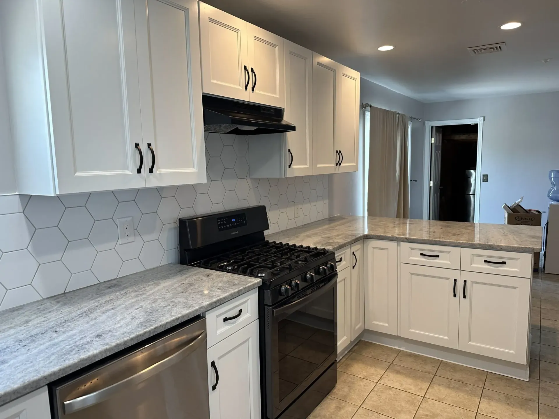 Bright modern kitchen with white cabinets, black stove, stainless dishwasher, and light countertops