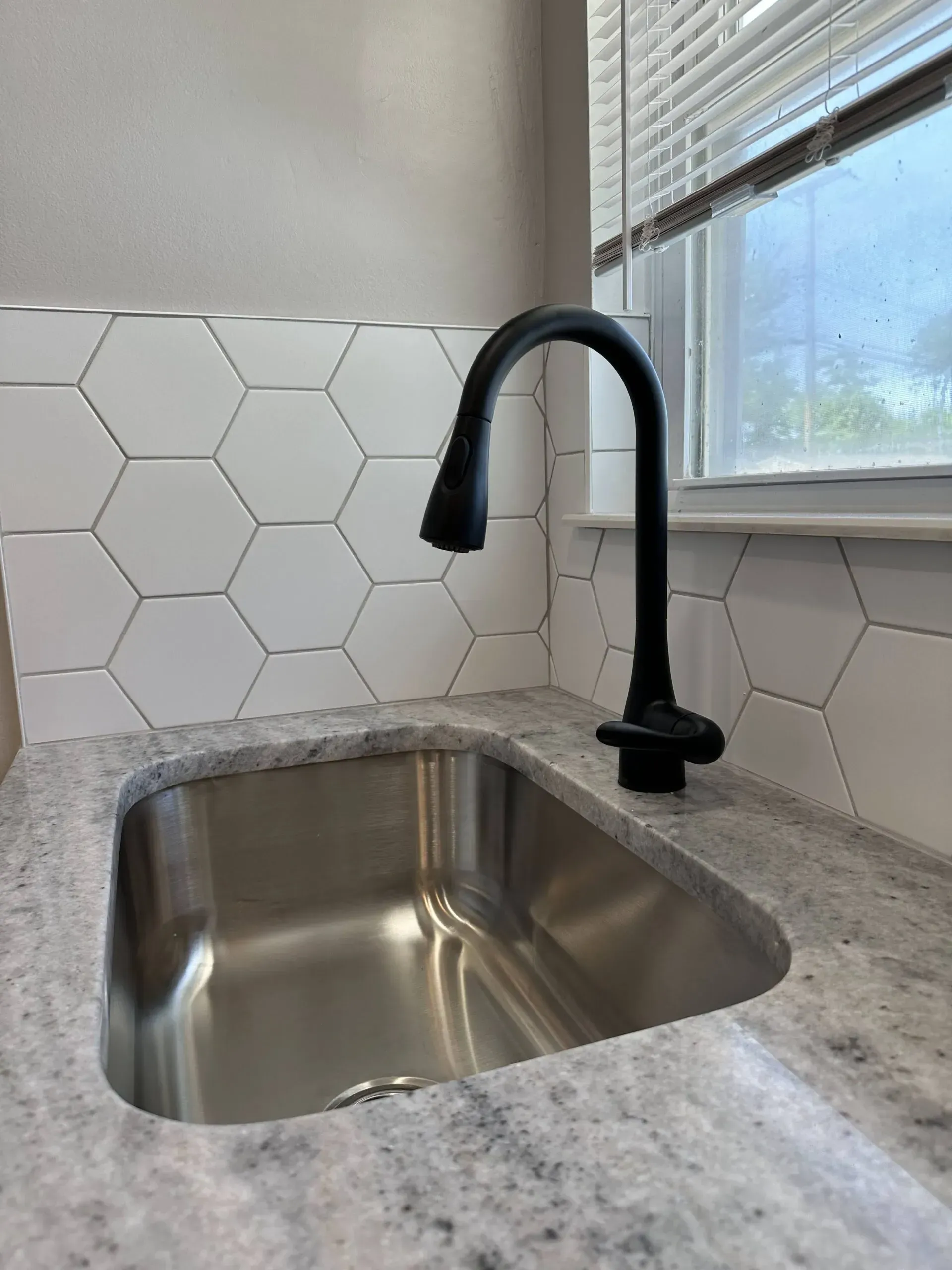 Modern kitchen sink with black gooseneck faucet, granite countertop, and white hex tile backsplash