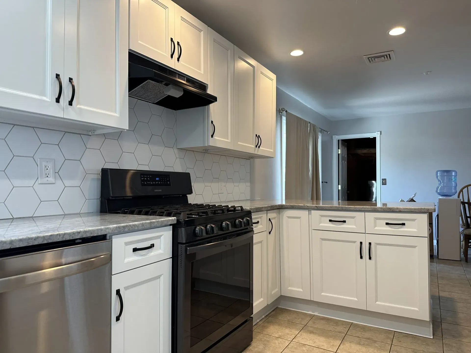 Bright white kitchen with stainless steel appliances, hexagon tile backsplash, and a center island