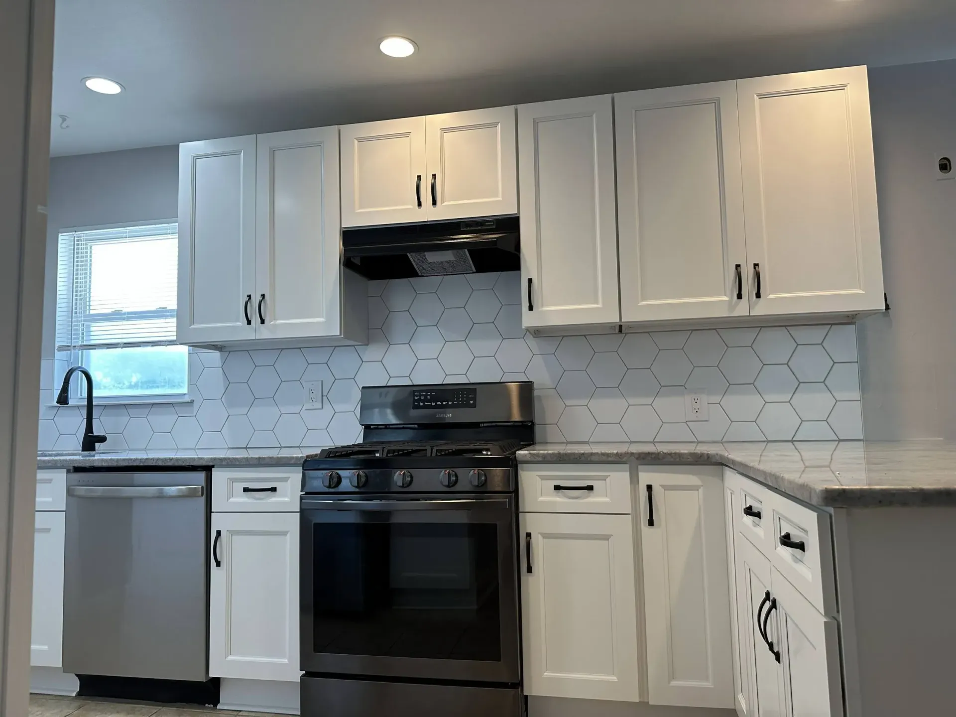 White kitchen with cabinets, black stove, stainless dishwasher, and hex tile backsplash